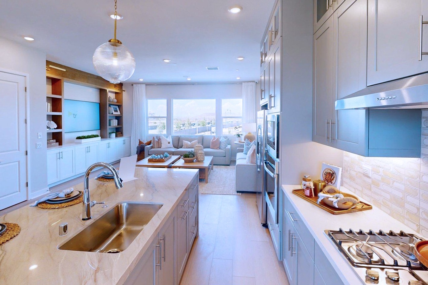 A modern kitchen island with a granite countertop and sink is in the foreground, while a spacious living room with large windows and comfortable seating is in the background.