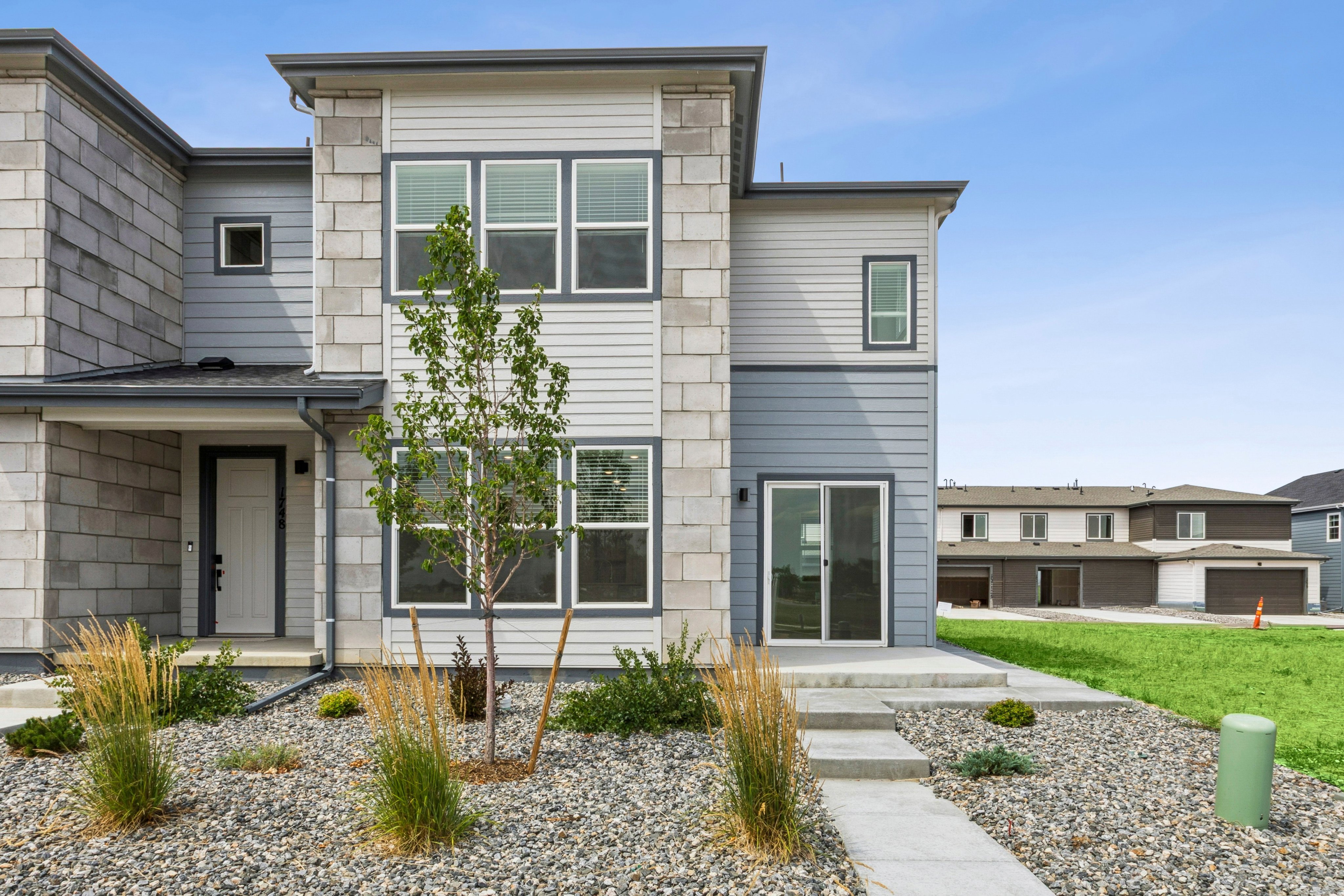 A modern townhouse with a gravel and grass yard in the foreground is set against a backdrop of similar homes under construction.