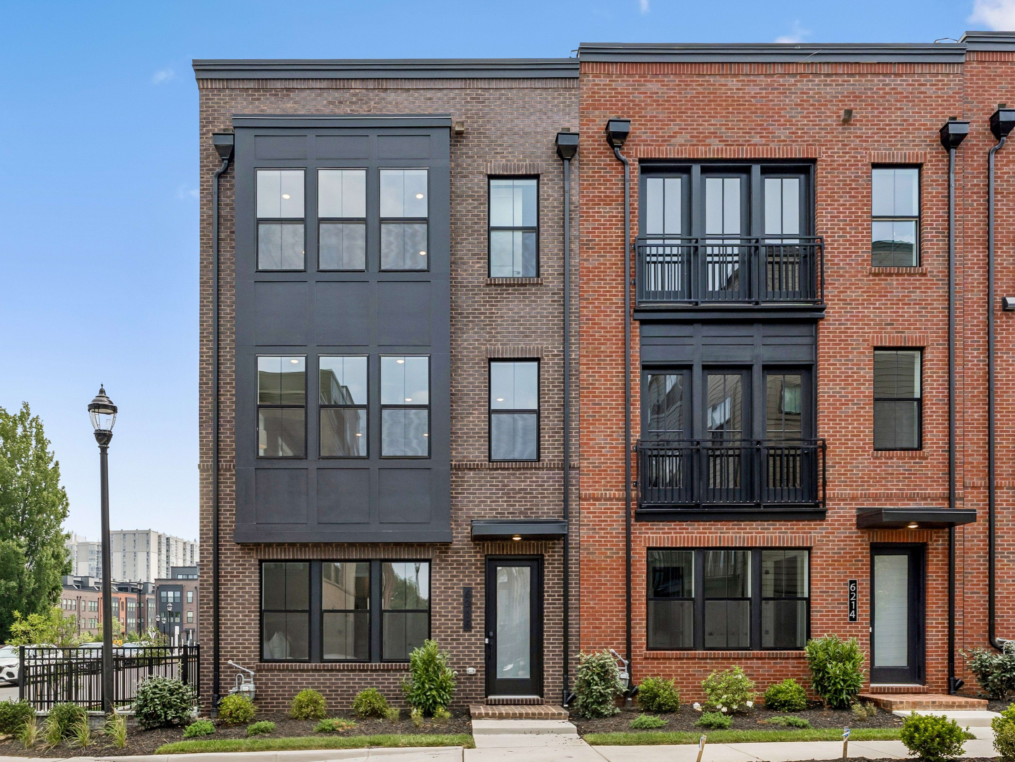 Modern brick townhouses with dark accents stand on a manicured lawn under a clear blue sky.