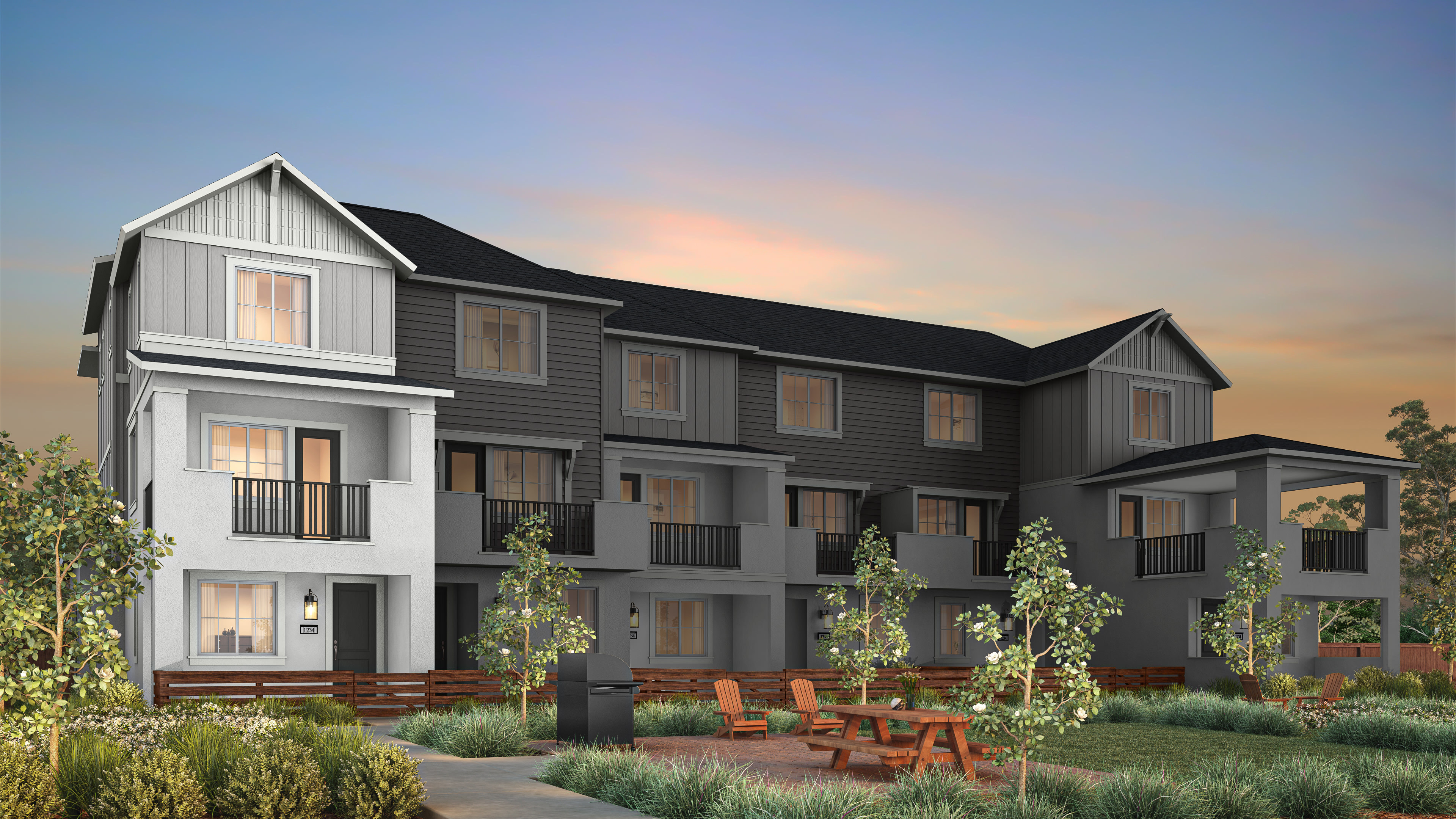 A modern, multi-story apartment building with a picnic table and chairs in the grassy foreground is set against a twilight sky.