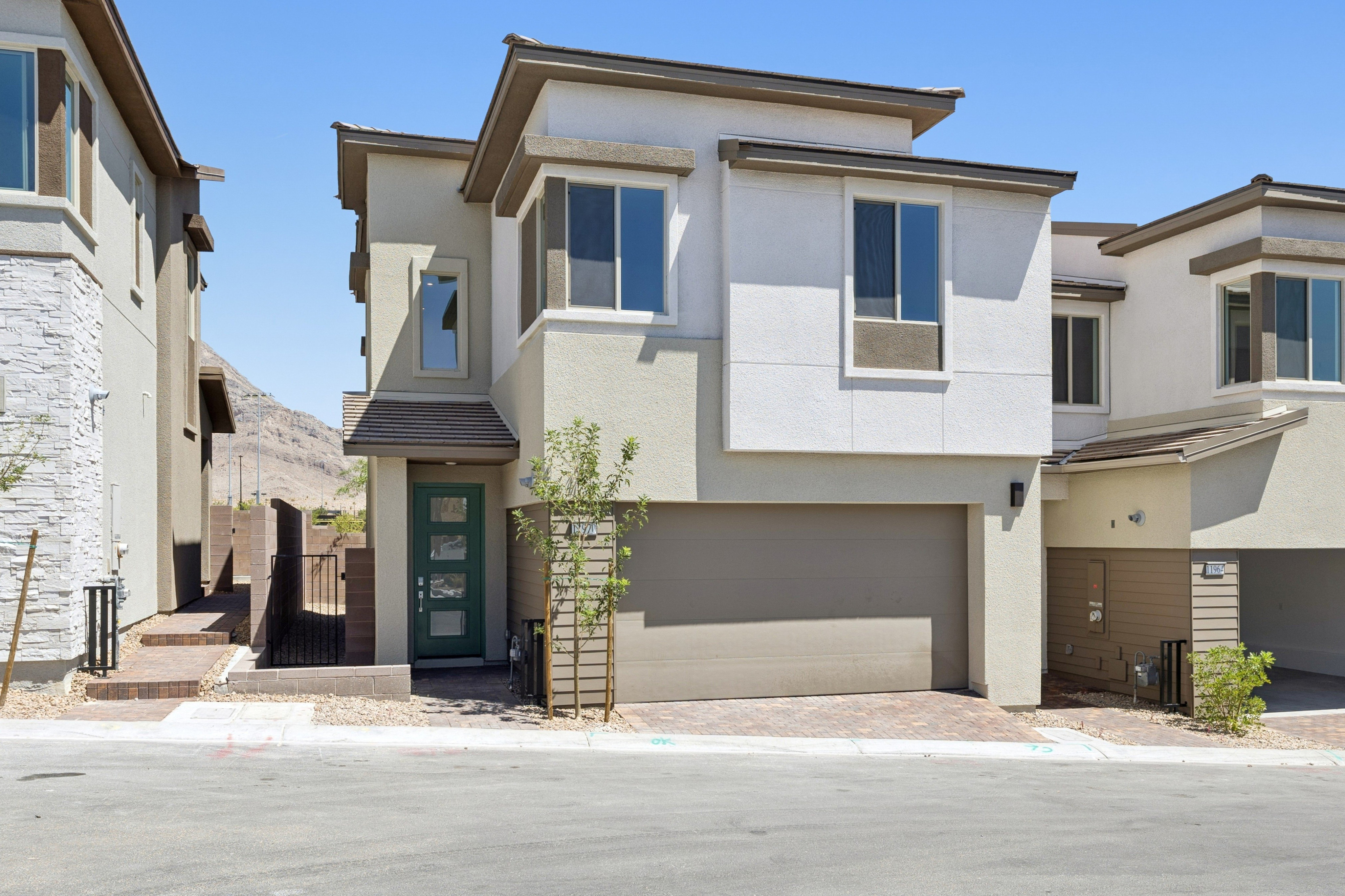 A modern townhouse with a green front door and garage is in the foreground, while a clear blue sky and distant hills form the background.