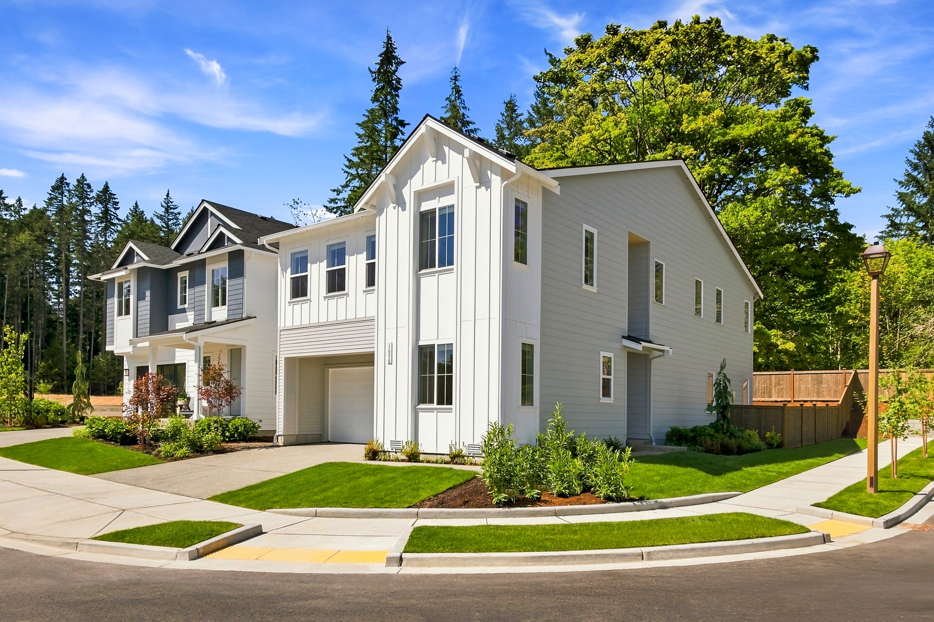 Modern townhouses with manicured lawns and sidewalks in the foreground are set against a backdrop of lush green trees and a bright blue sky.