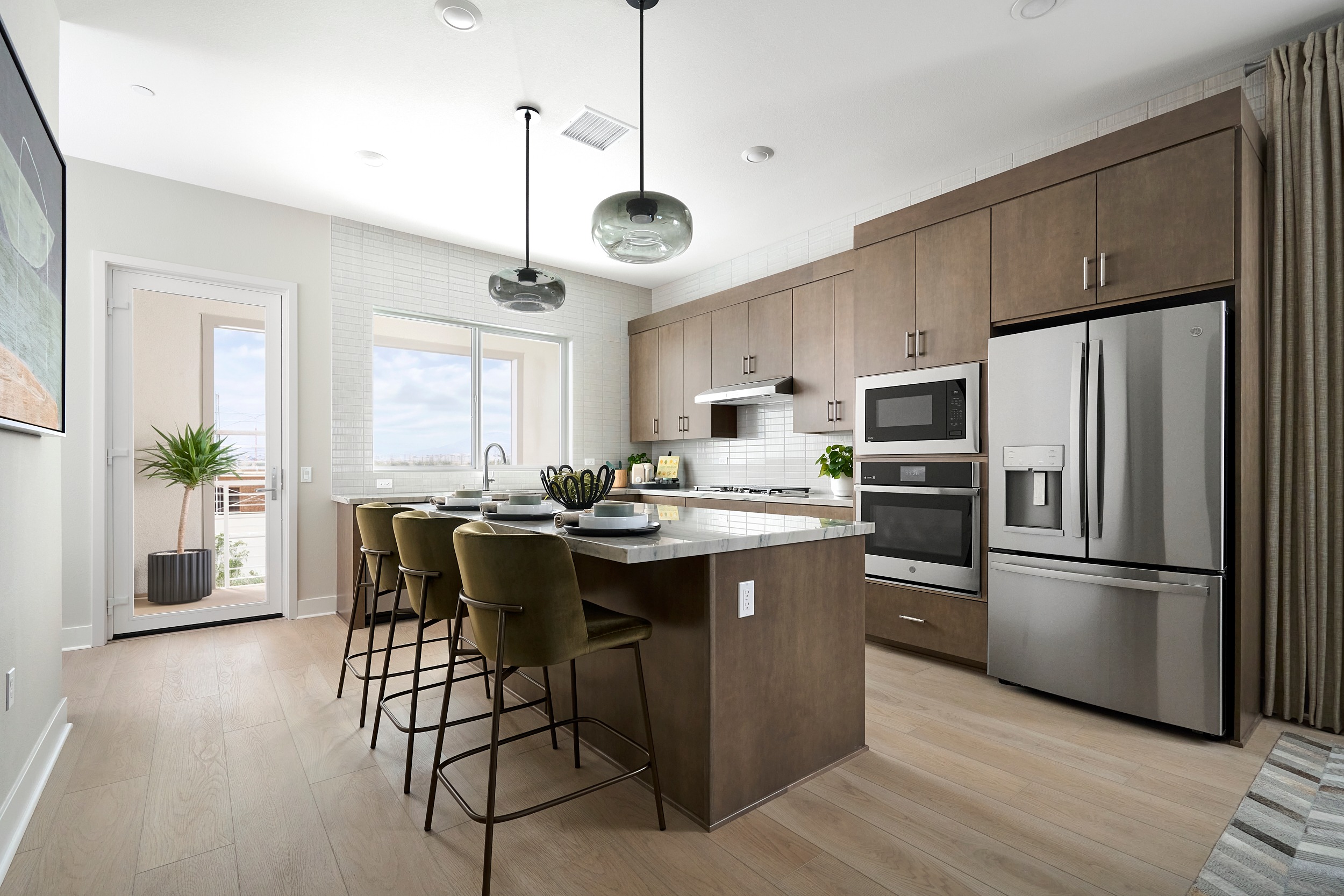 A modern kitchen with a large island in the foreground and stainless steel appliances and cabinetry in the background.