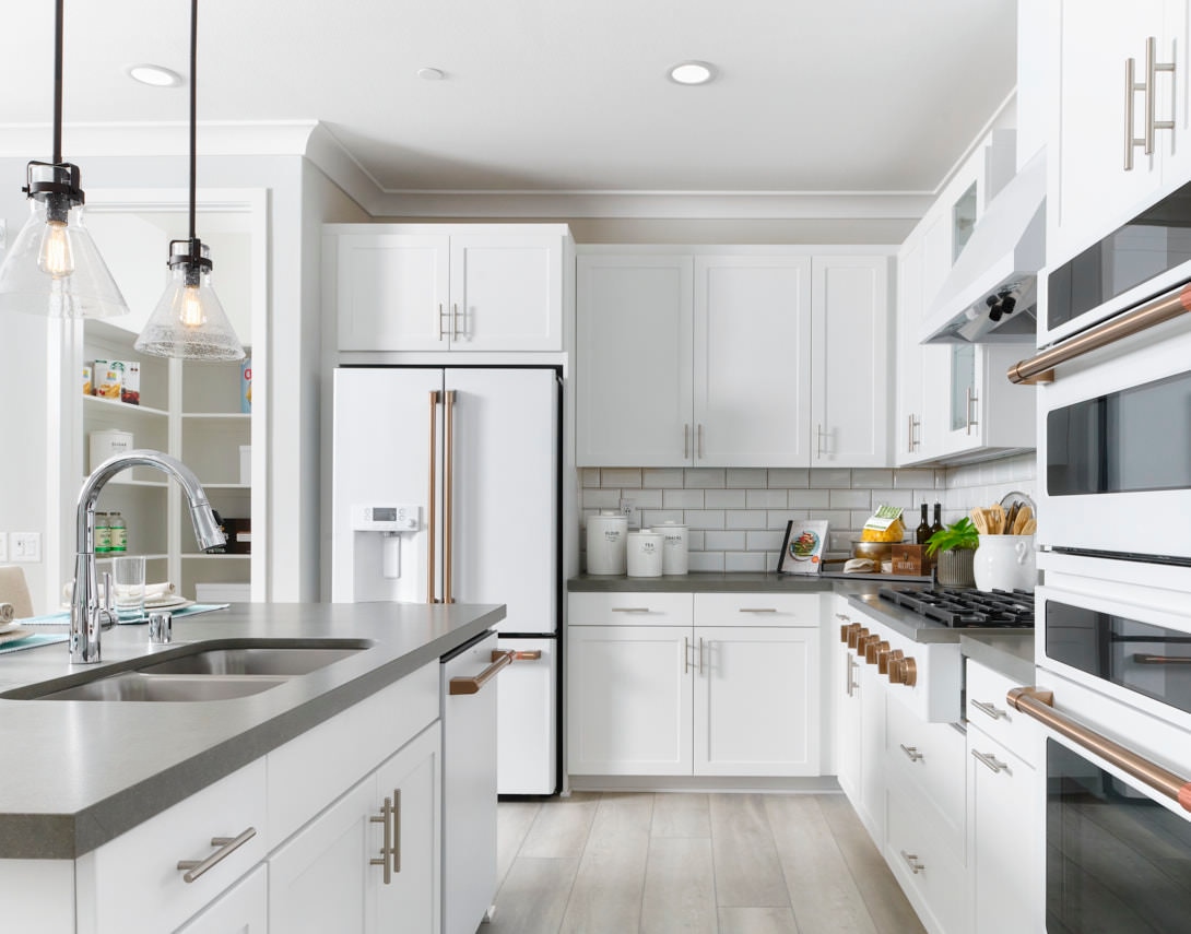 A modern white kitchen with a large island in the foreground and white cabinets and appliances in the background.