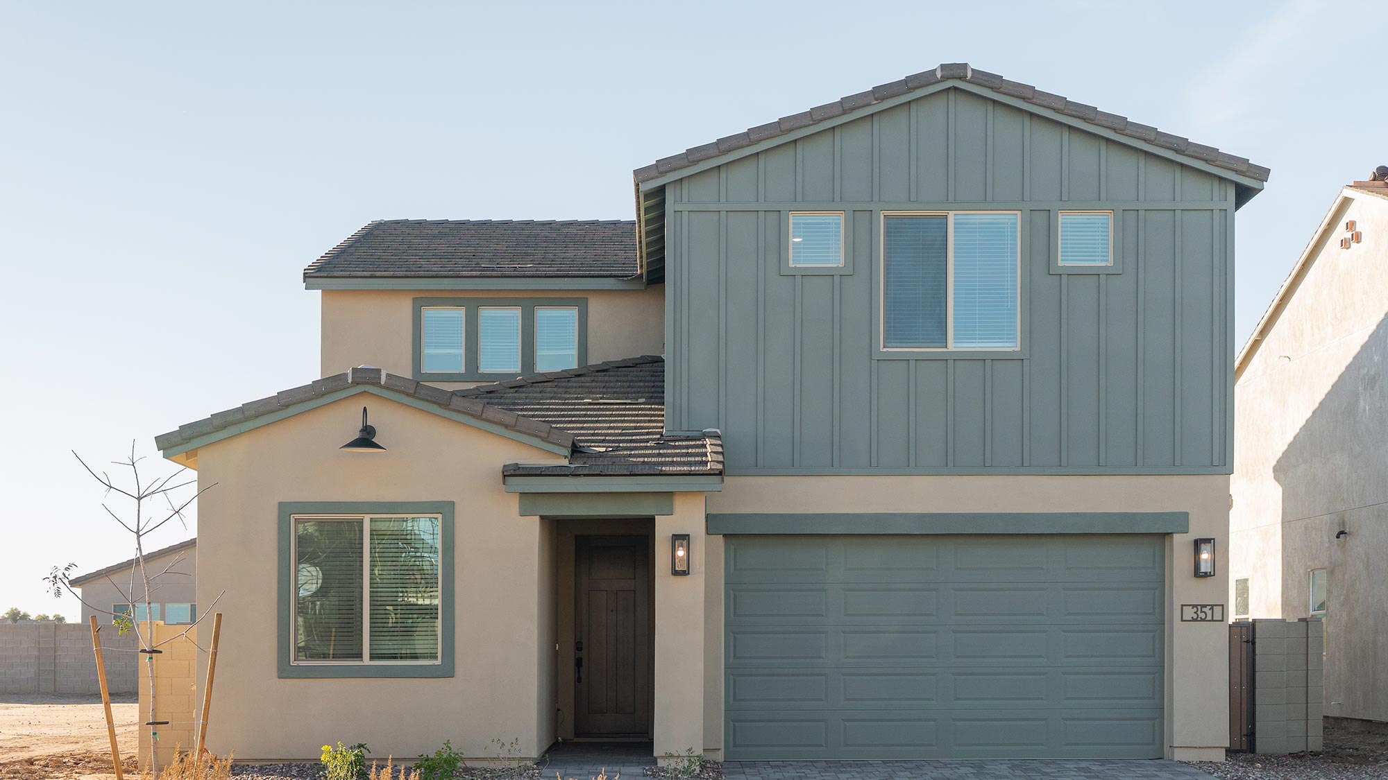 A modern two-story house with beige and sage green siding stands under a clear, pale blue sky.