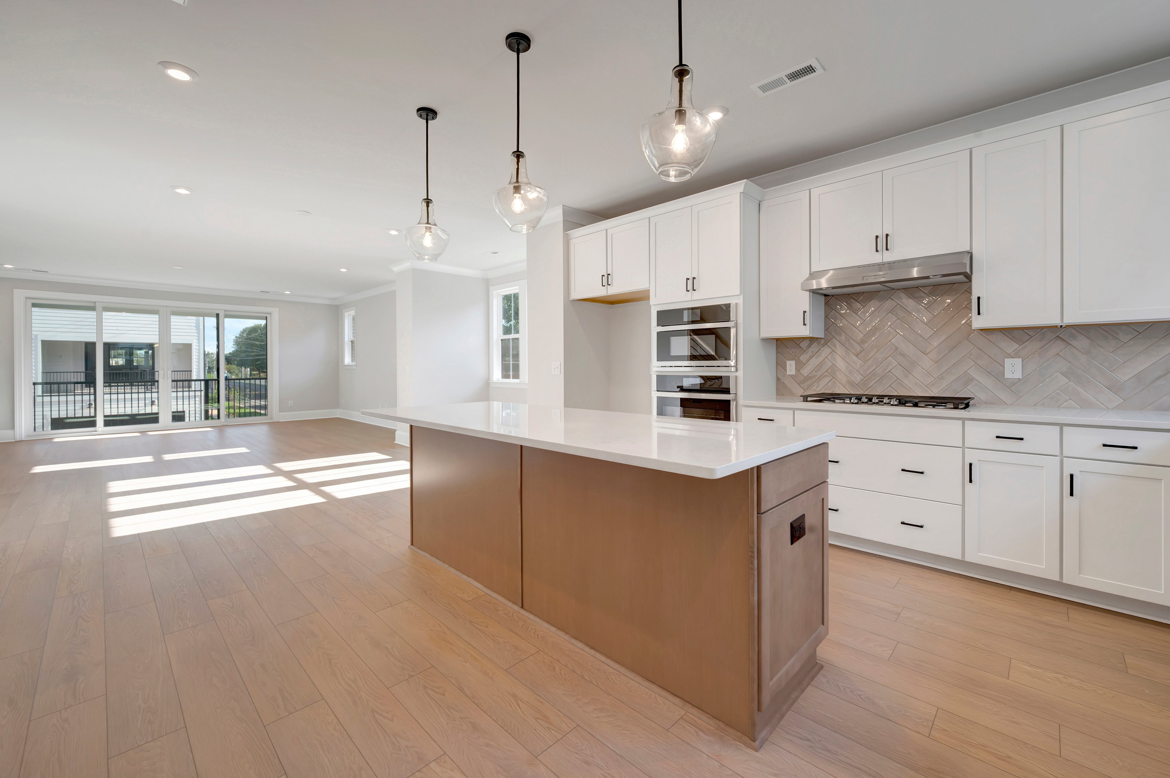 A modern kitchen features a large wooden island with a white countertop in the foreground and white cabinetry with a herringbone backsplash in the background.