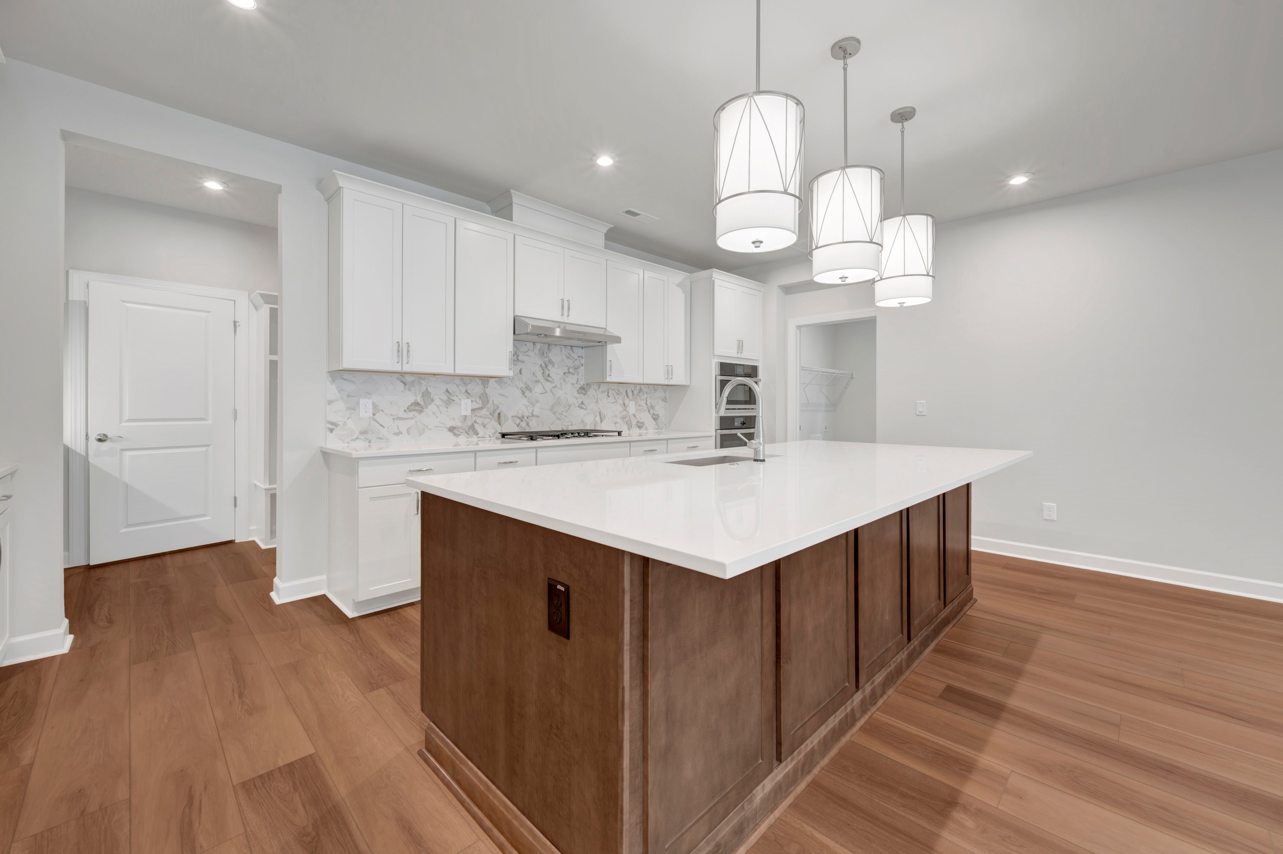 A large kitchen island with a white countertop and wood base sits in the foreground of a modern white kitchen with hardwood floors.