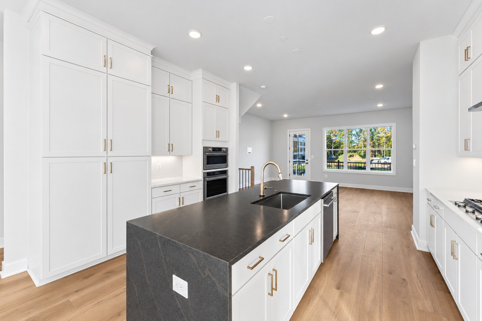 A modern kitchen features a large black island with a gold faucet in the foreground and white cabinetry with gold hardware against a light-colored wall in the background.