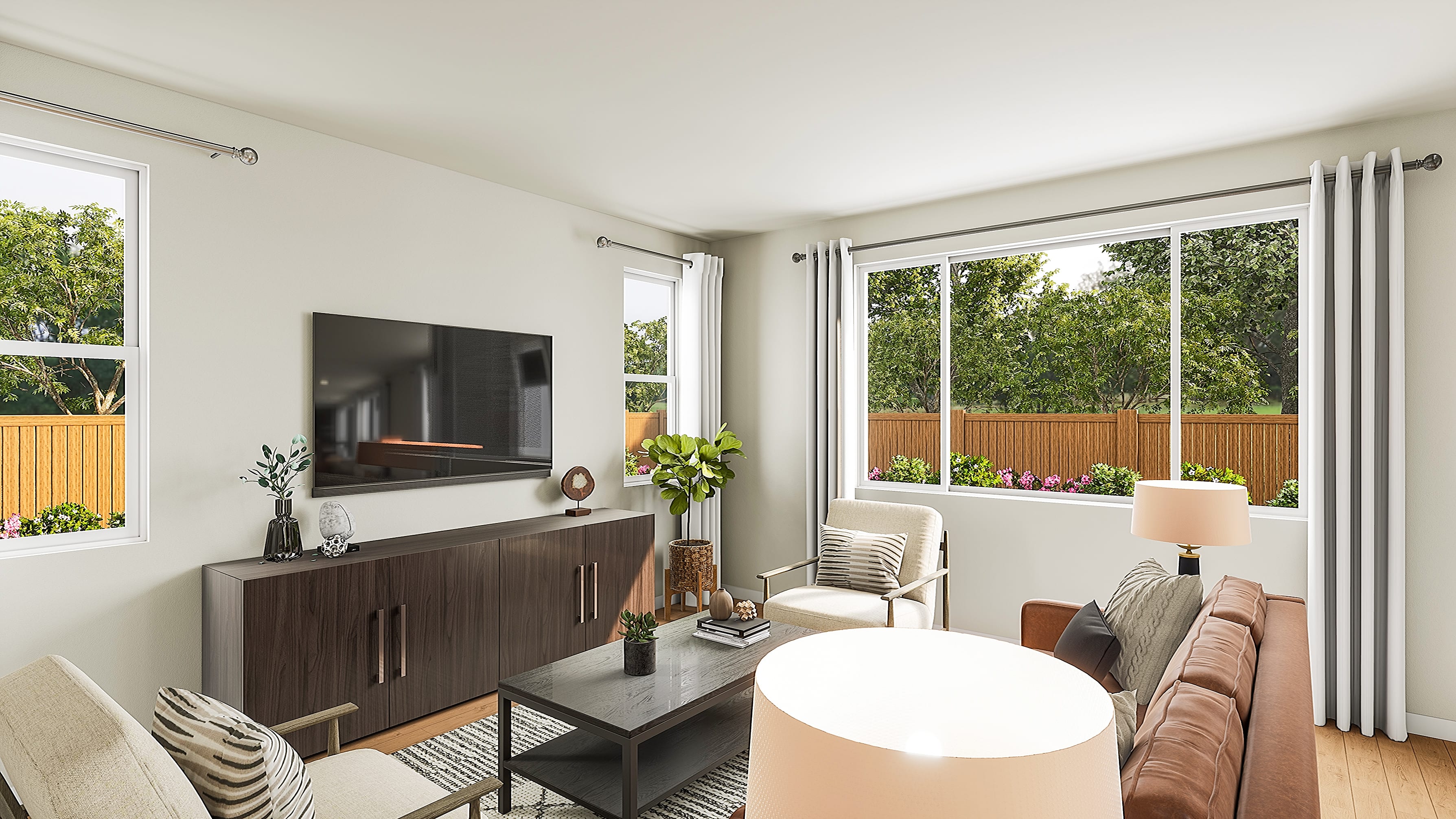 A modern living room with a dark wood media console and coffee table in the foreground, and large windows revealing a backyard with lush greenery and a wooden fence in the background.