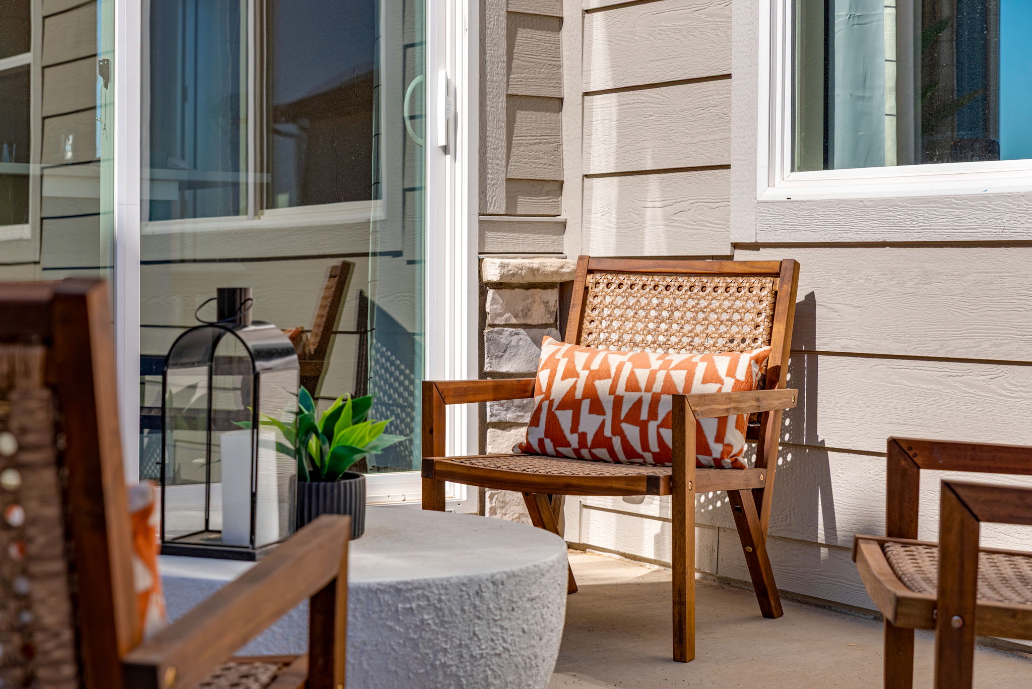 A cozy outdoor seating area with a wooden chair adorned with a patterned cushion, surrounded by a glass-paneled entryway and a potted plant, creating a welcoming and inviting atmosphere.