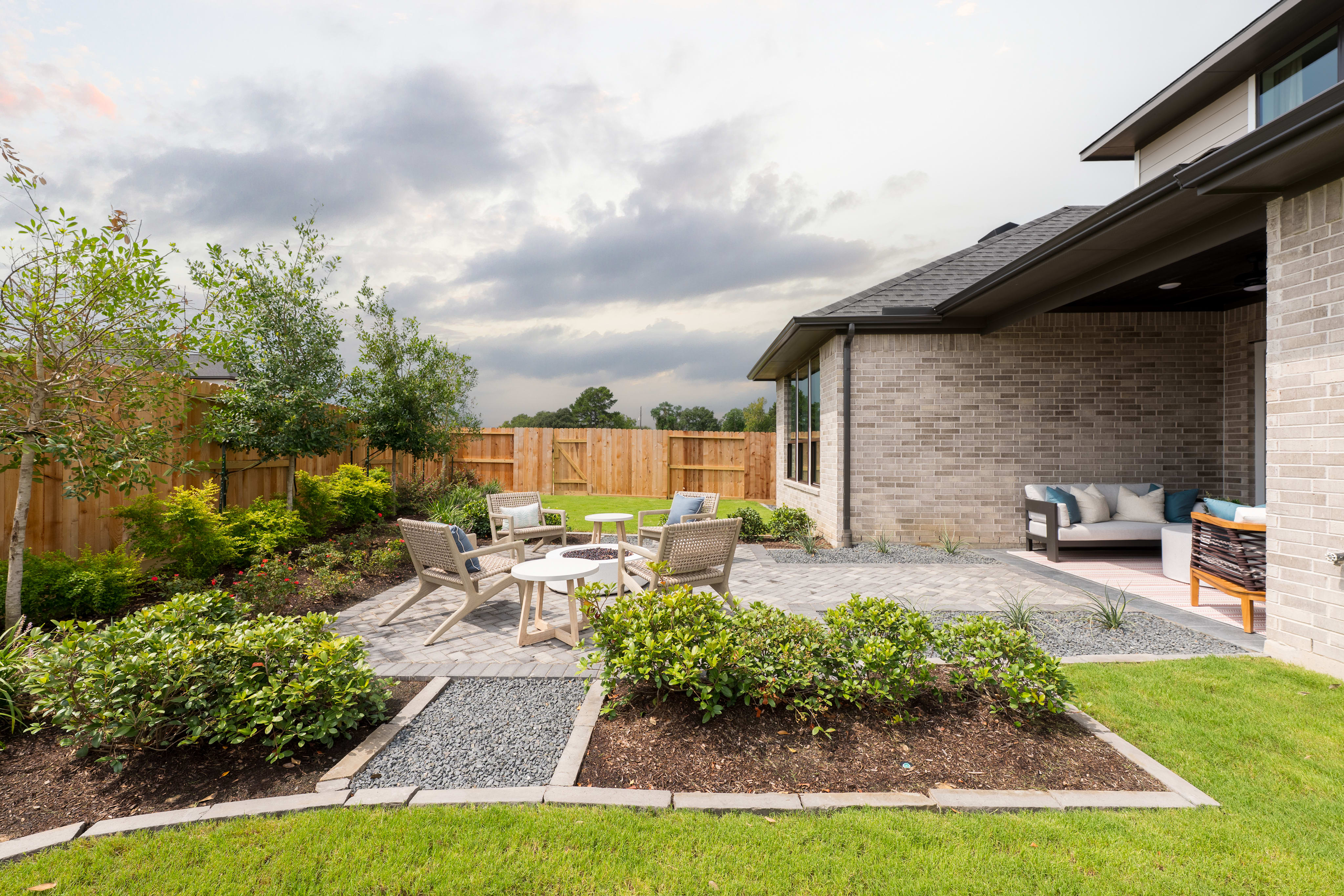 A well-designed outdoor living space with a patio, seating area, and lush landscaping, set against a backdrop of a residential home with a cloudy sky overhead.