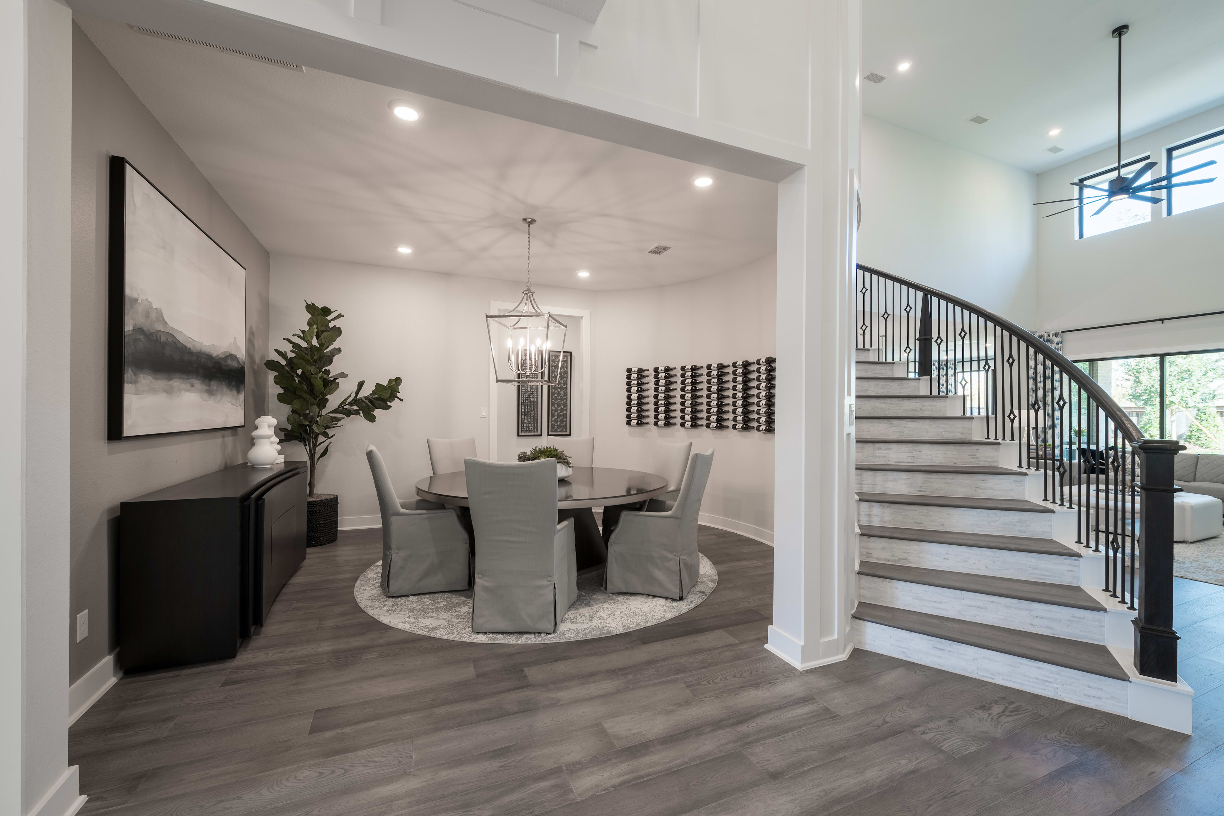 A modern and elegant dining area with a circular table and chairs, surrounded by a staircase and various decor elements in a spacious, well-lit interior.