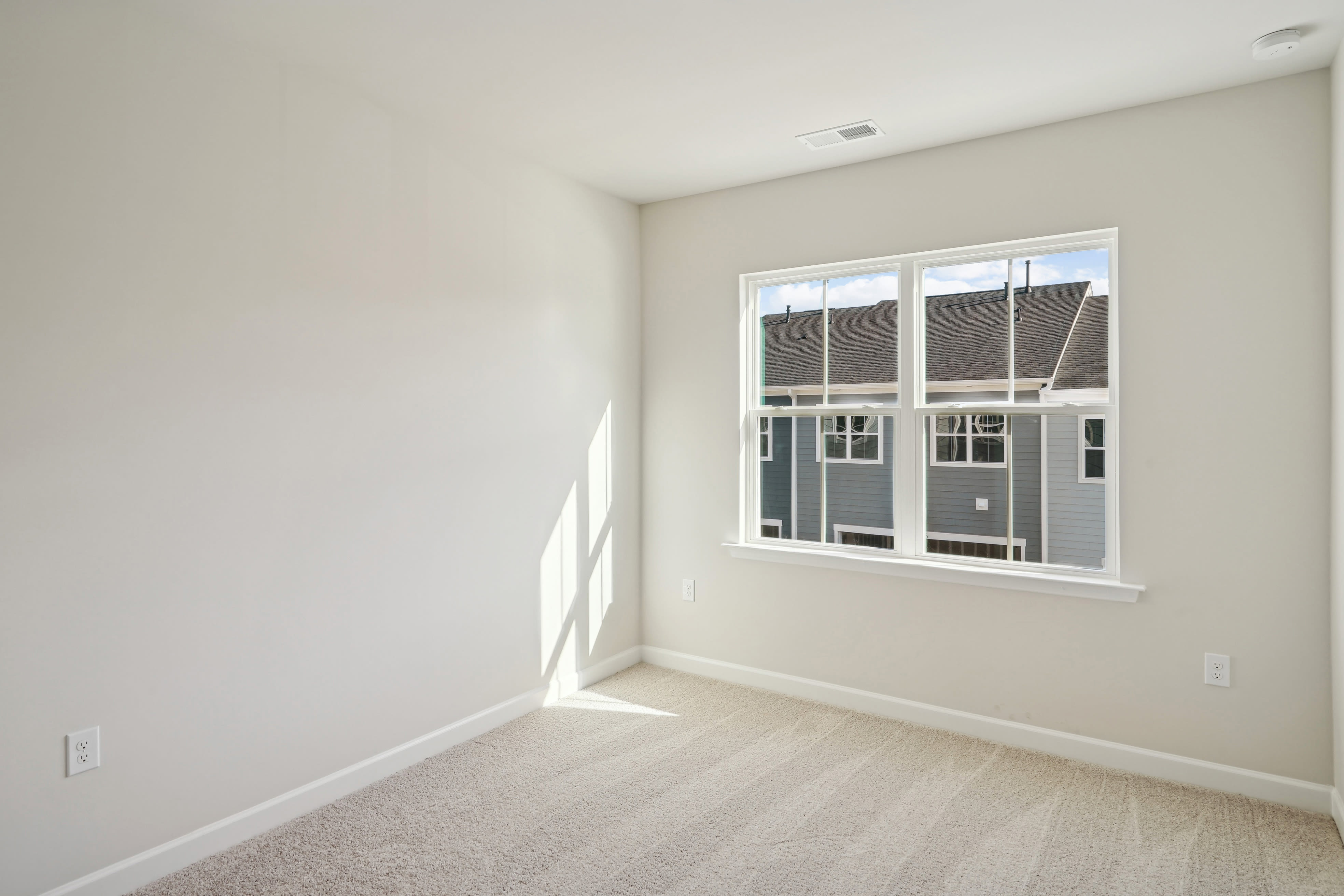 An empty, well-lit room with a large window, hardwood floors, and neutral-colored walls.