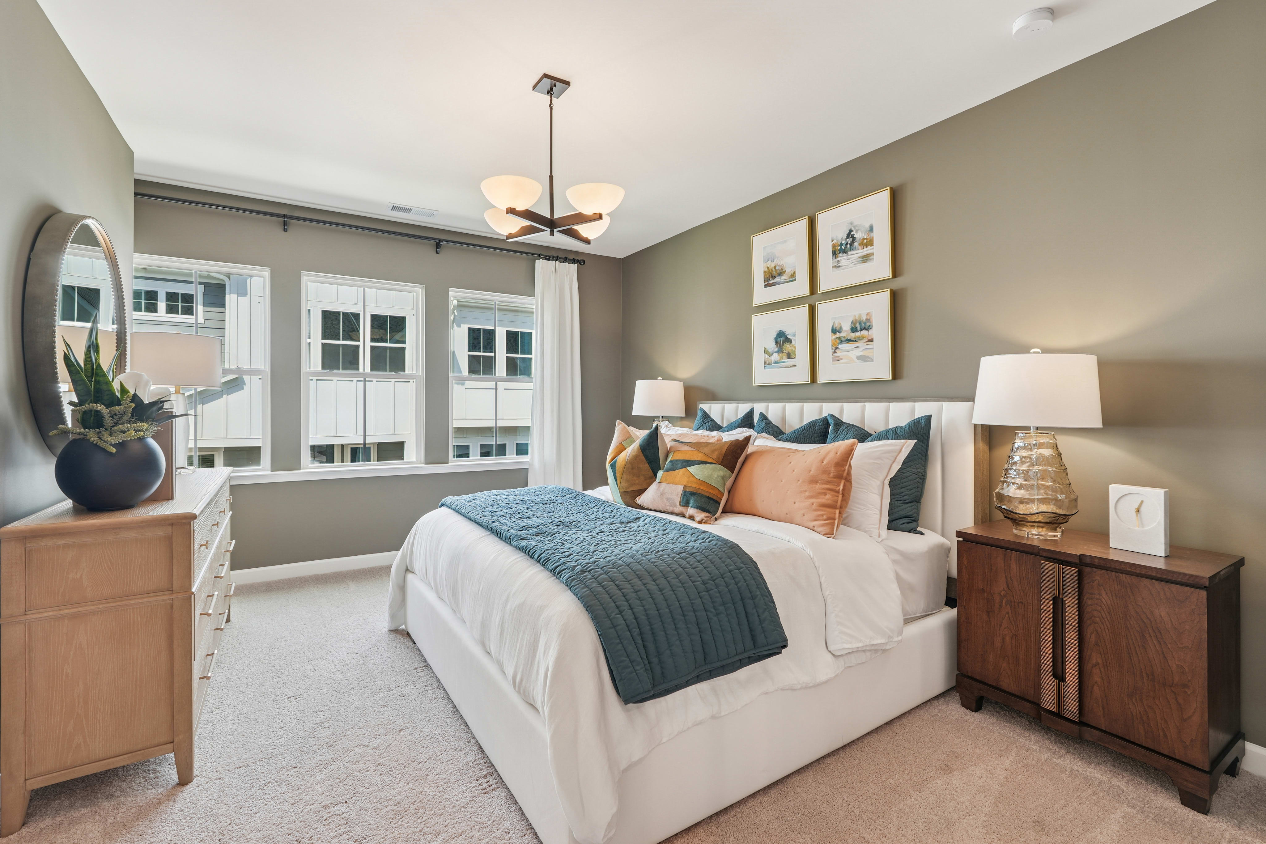 A cozy and well-decorated bedroom with a large bed, wooden furniture, and framed artwork on the walls, surrounded by large windows that let in natural light.