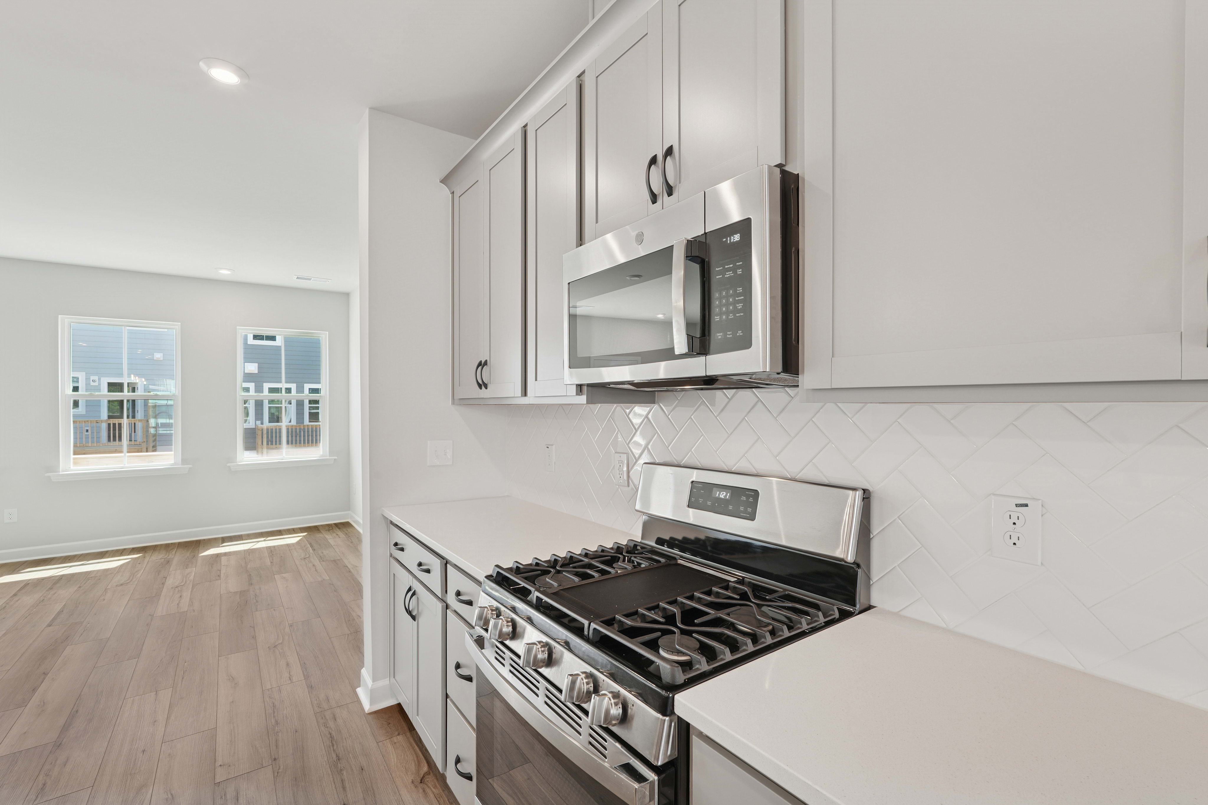 A modern, well-equipped kitchen with white cabinets, a gas stove, and a microwave oven, set against a backdrop of a bright, open living space with hardwood floors.