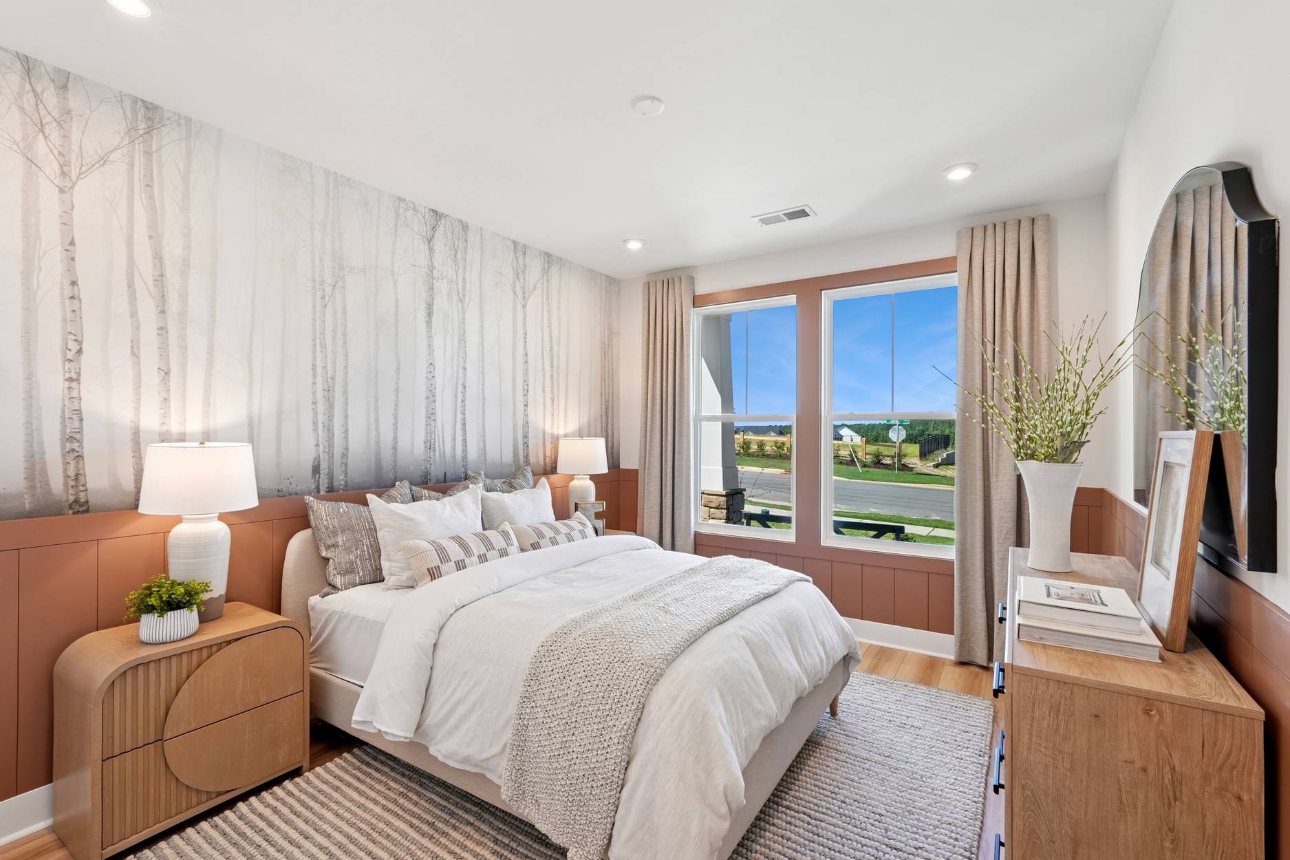 A cozy and modern bedroom with a large window overlooking a scenic outdoor landscape, featuring a plush bed, wooden furniture, and neutral-toned decor.