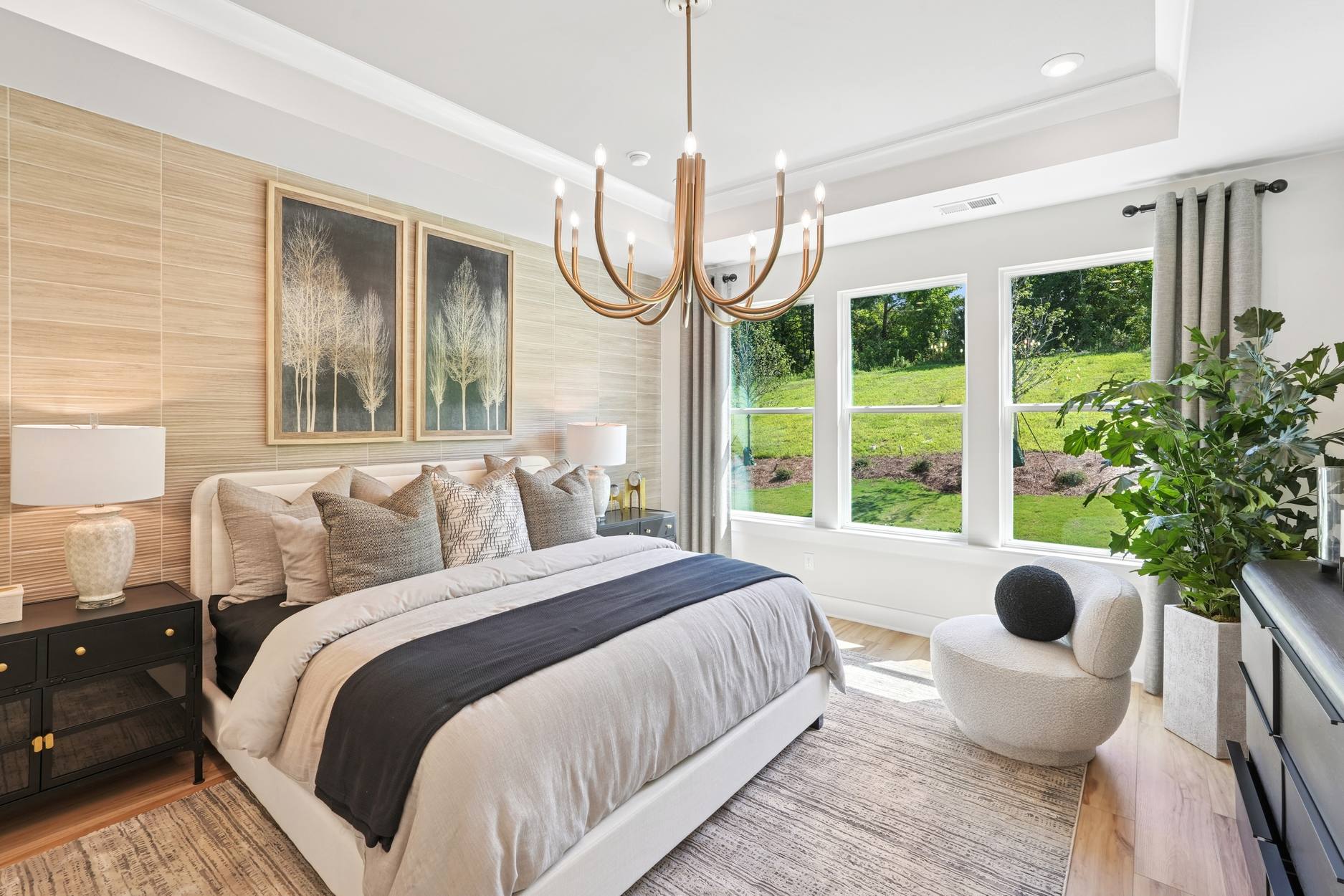A cozy and inviting bedroom with a large window overlooking a lush, green outdoor landscape, featuring a plush bed, wooden accents, and a stylish chandelier.