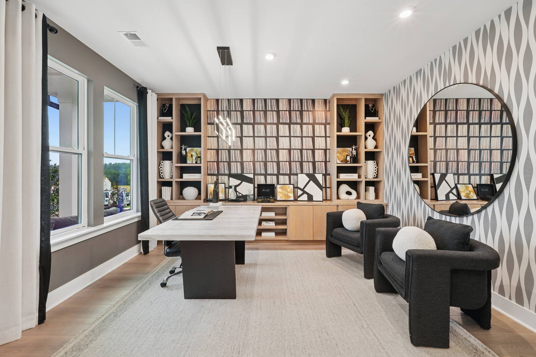 A modern and stylish home office space with a large wooden desk, comfortable armchairs, and a wall-mounted shelving unit filled with various decorative items.