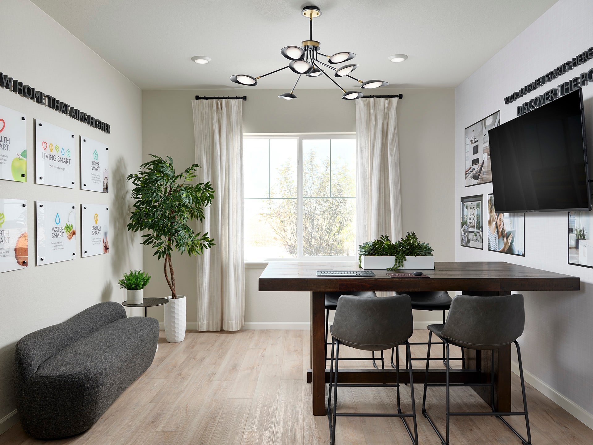 A modern and minimalist home office space with a wooden dining table, gray chairs, and a large window providing natural light, surrounded by plants and wall decor.