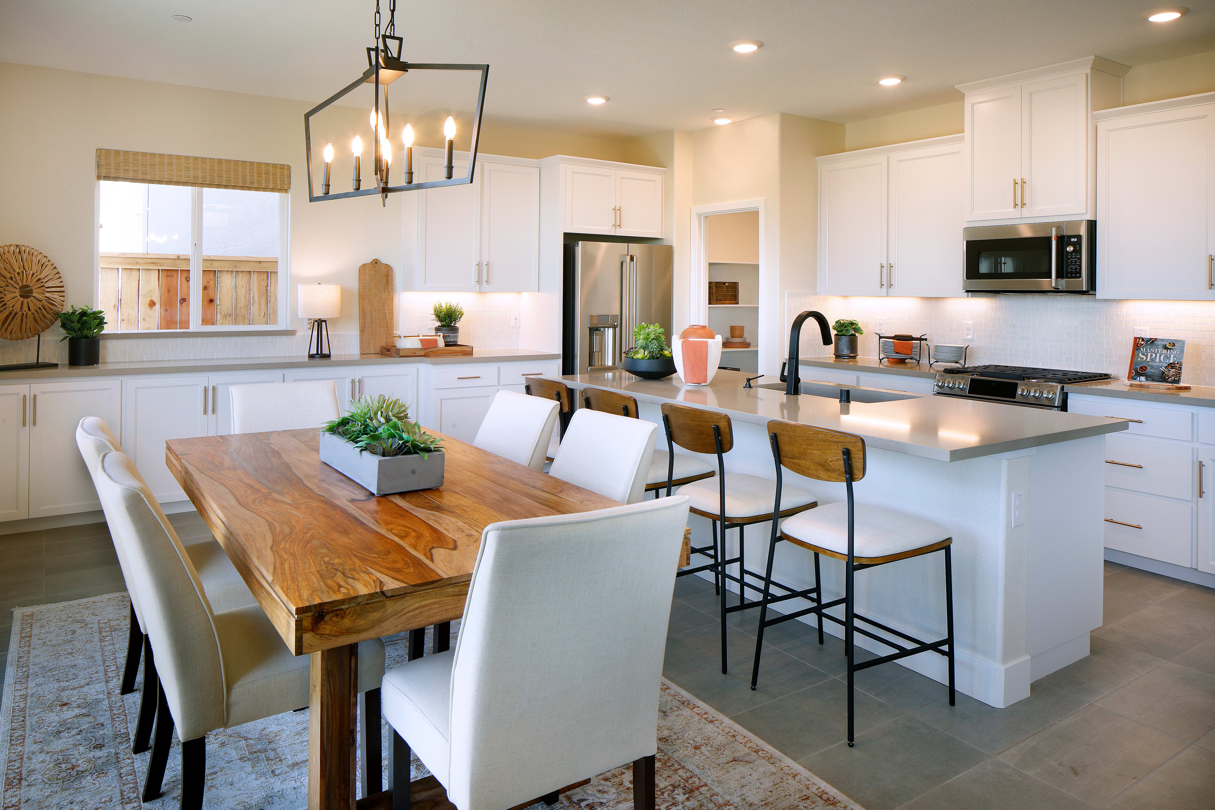 A modern and spacious kitchen with a wooden dining table, white cabinets, and a central island with bar stools, all illuminated by a stylish pendant light fixture.