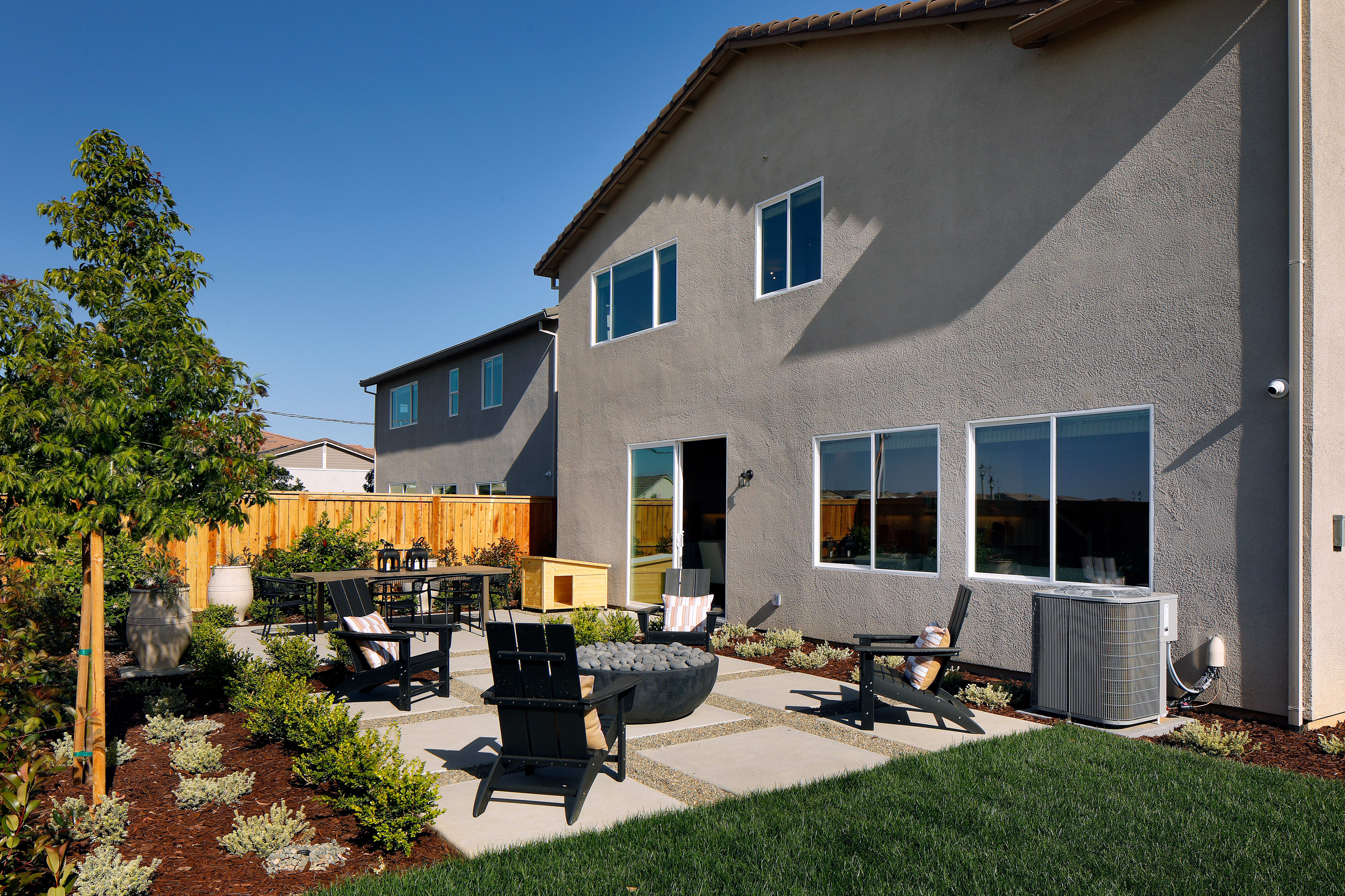 A well-maintained residential property with a patio area featuring outdoor furniture, surrounded by a lush green lawn and landscaping, with a two-story house in the background.