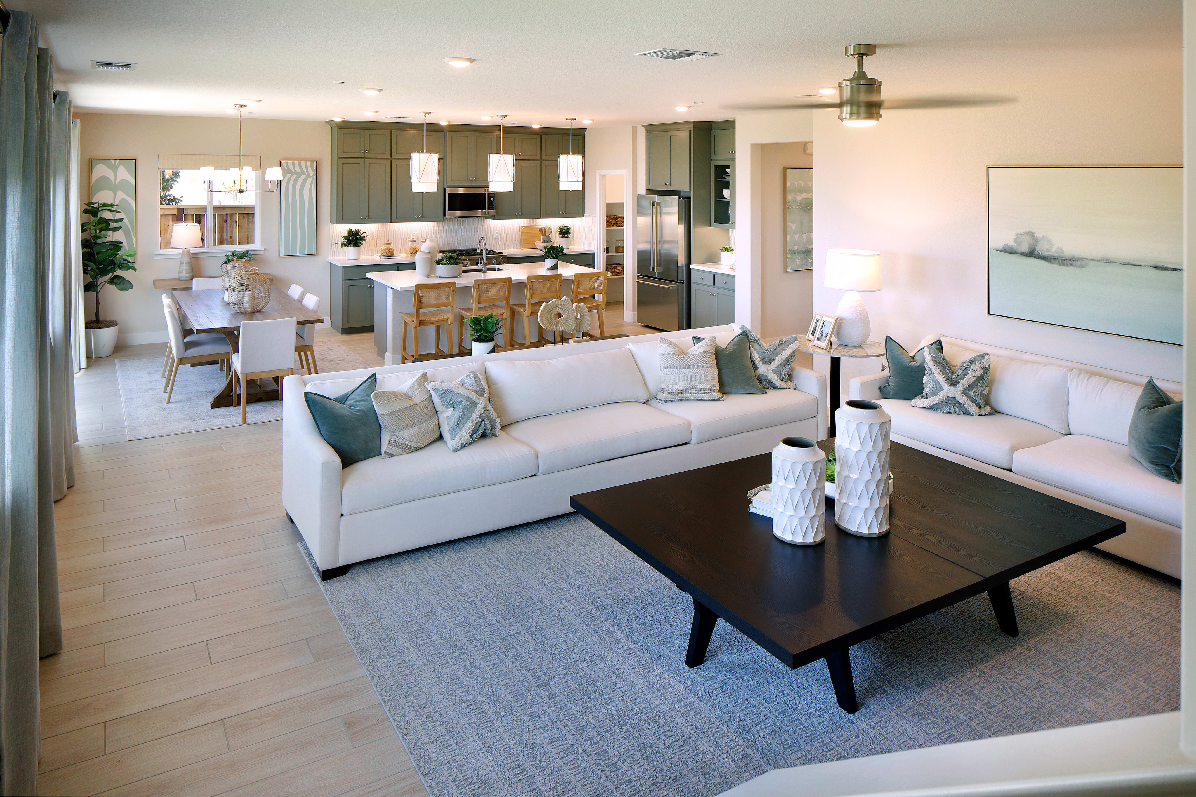 A spacious and modern open-plan living room with a comfortable white sofa, a large coffee table, and a well-equipped kitchen visible in the background.