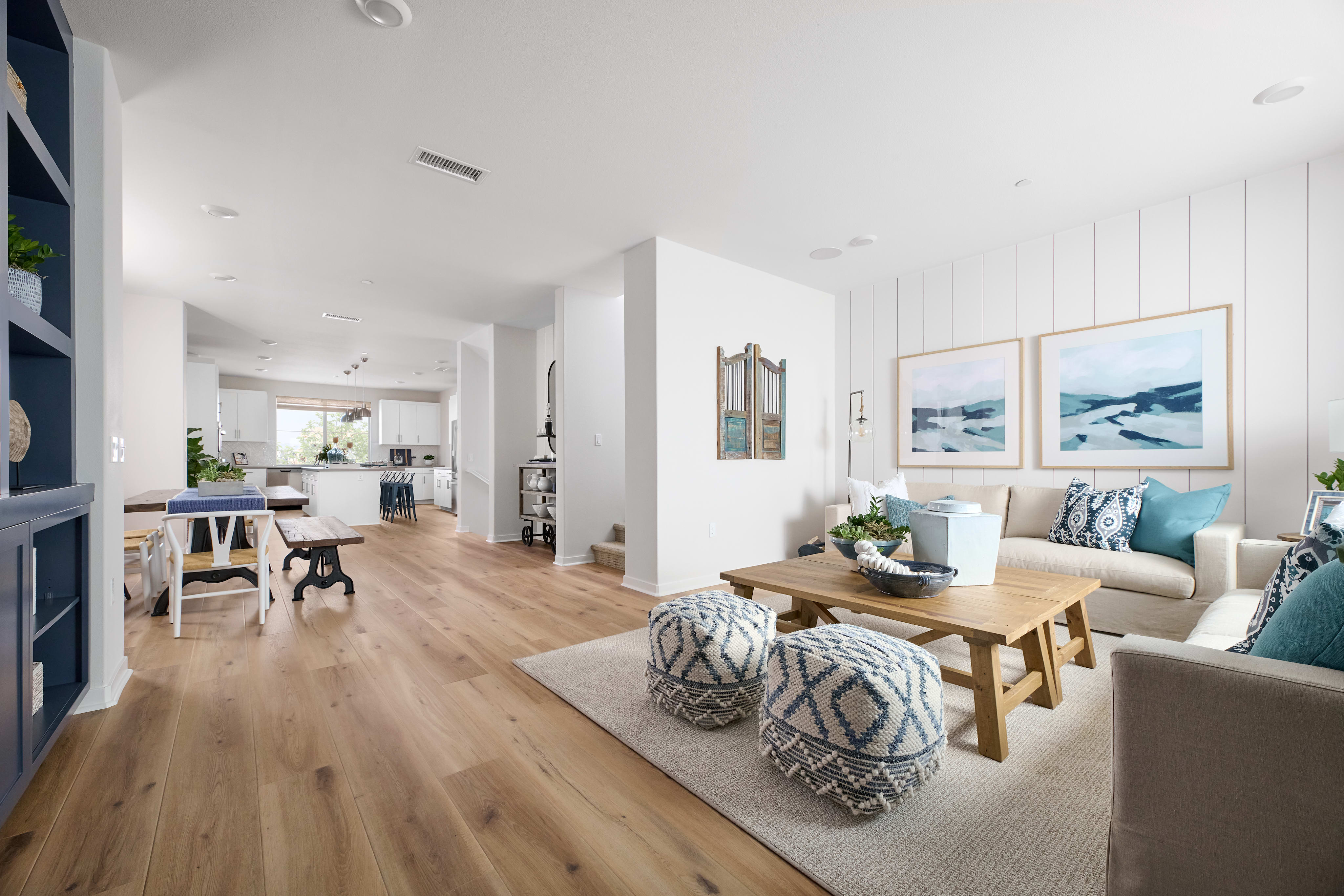A bright and airy open-concept living space with a cozy seating area, wooden dining table, and a glimpse of the kitchen in the background.