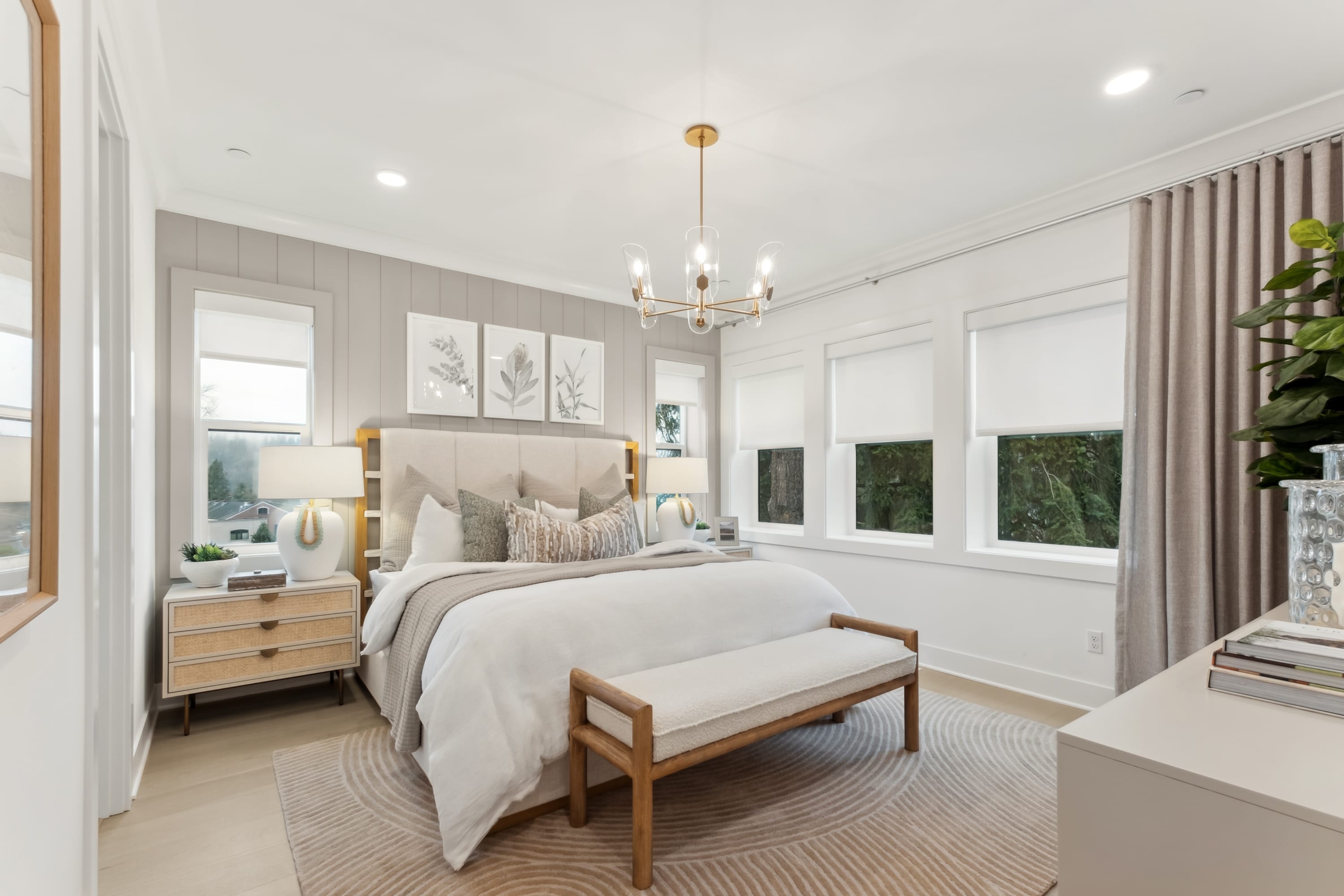 A cozy and well-designed bedroom with a large bed, wooden furniture, and decorative elements, set against a backdrop of large windows overlooking a lush outdoor environment.