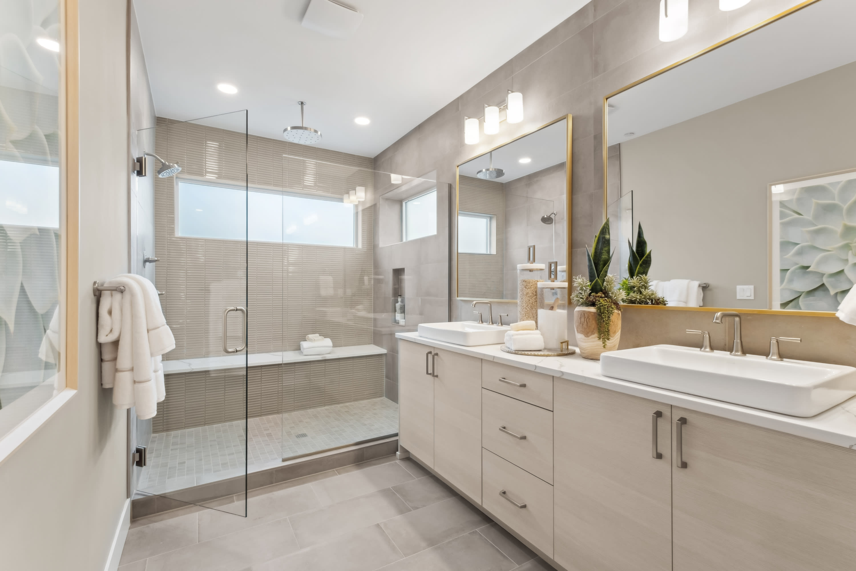 A modern and spacious bathroom with a large glass shower enclosure, a vanity with drawers, and various decorative elements such as plants and towels.