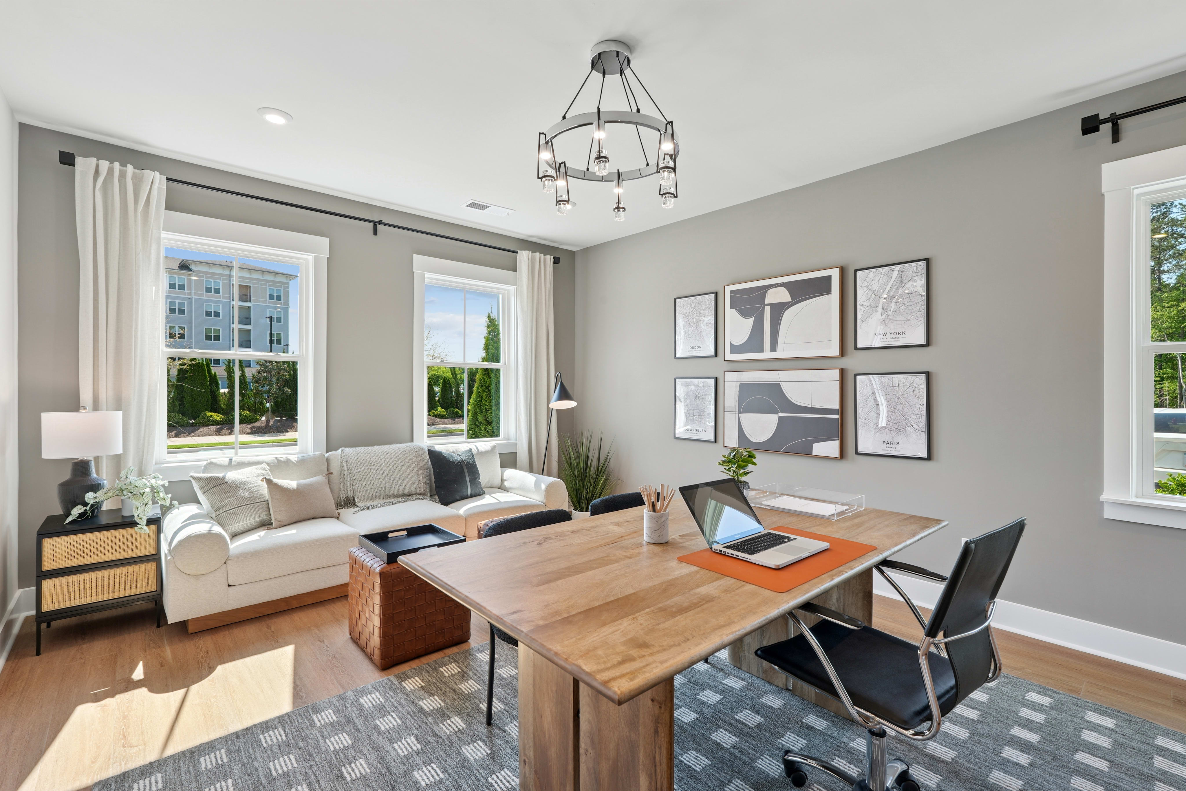A cozy and well-furnished living room with a wooden dining table, comfortable seating, and artwork on the walls, overlooking a scenic outdoor view through the large windows.