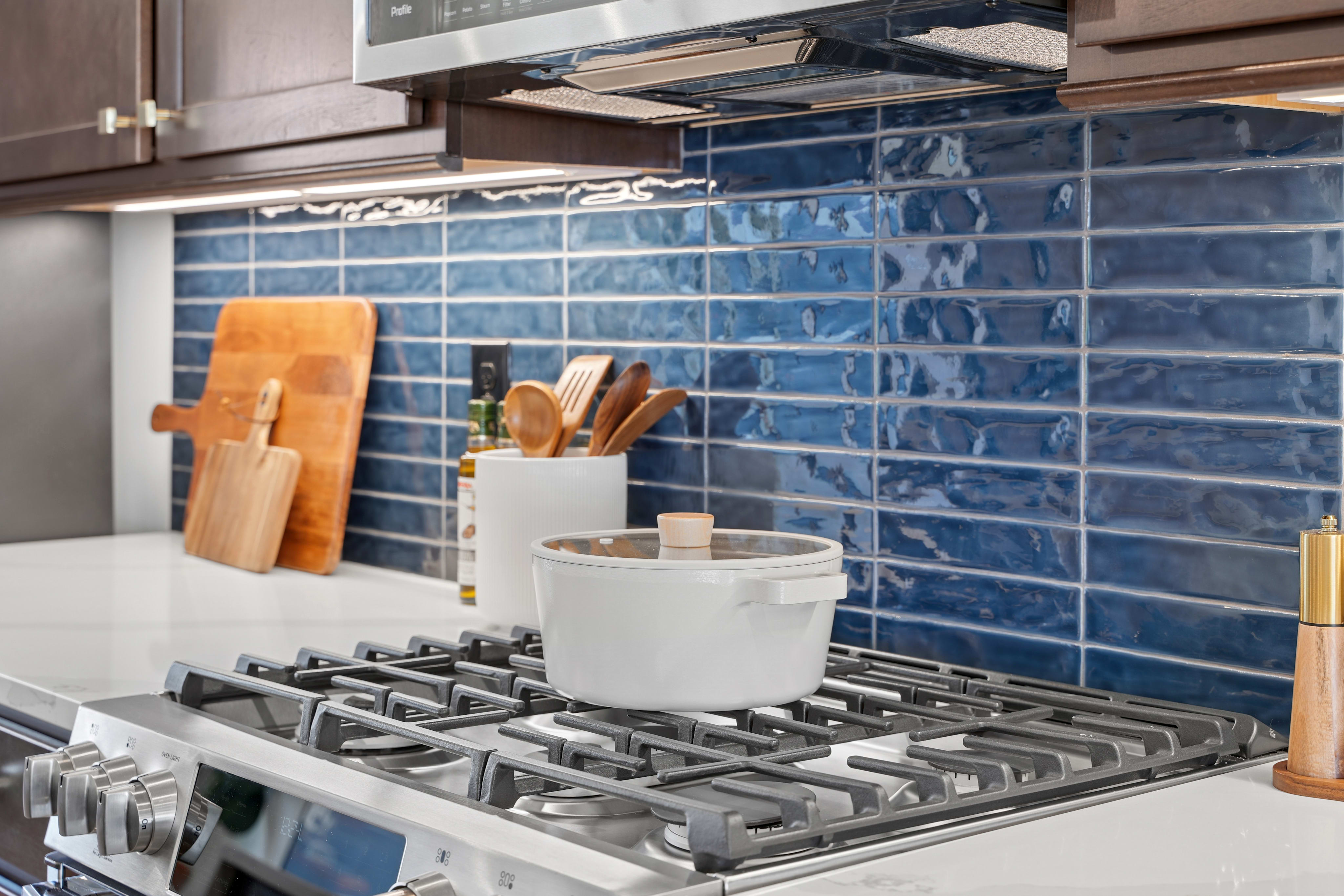The image shows a kitchen countertop with a gas stove, various cooking utensils, and a backsplash of blue ceramic tiles.