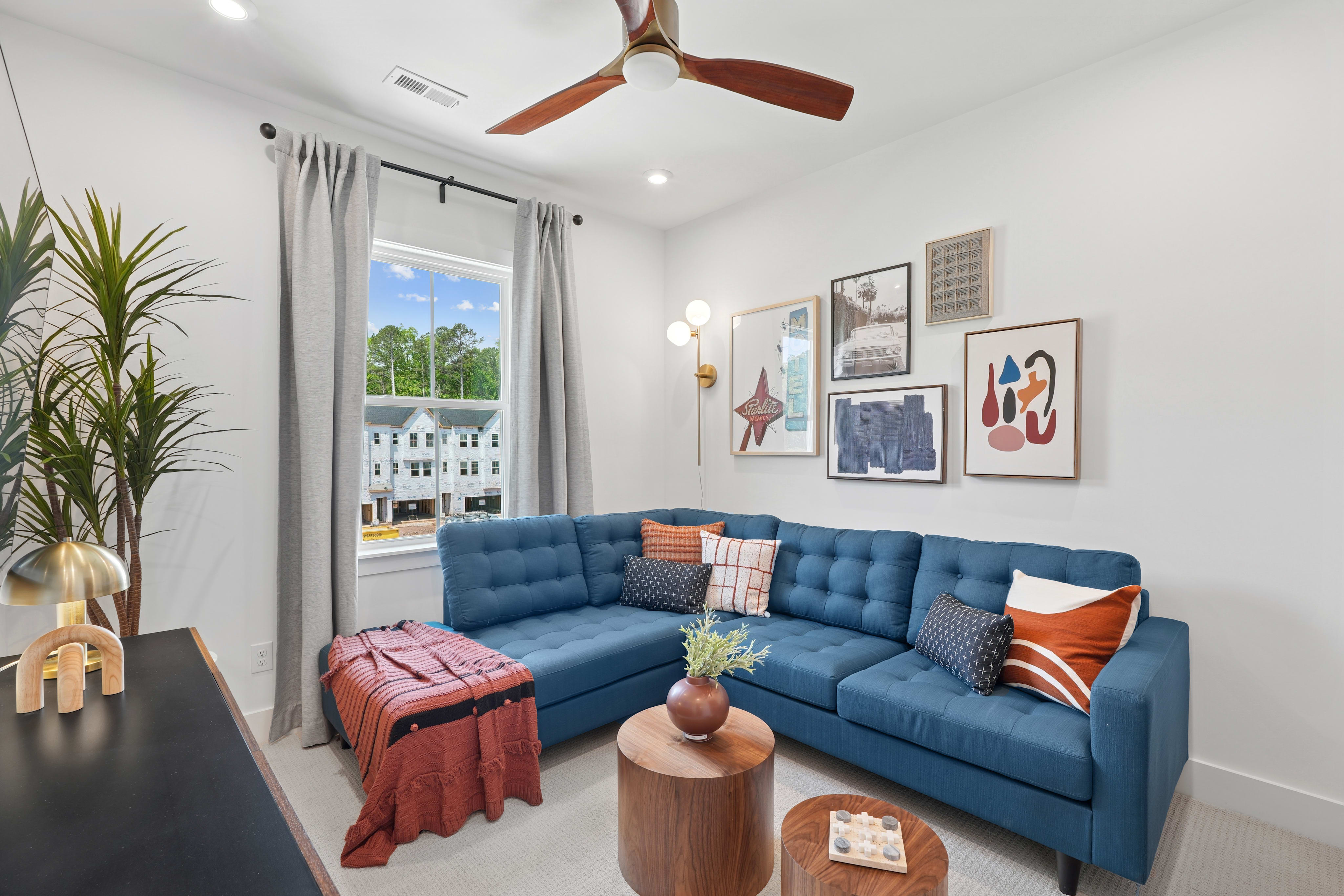 A cozy and vibrant living room with a blue sectional sofa, colorful artwork on the walls, and a ceiling fan providing a comfortable atmosphere.