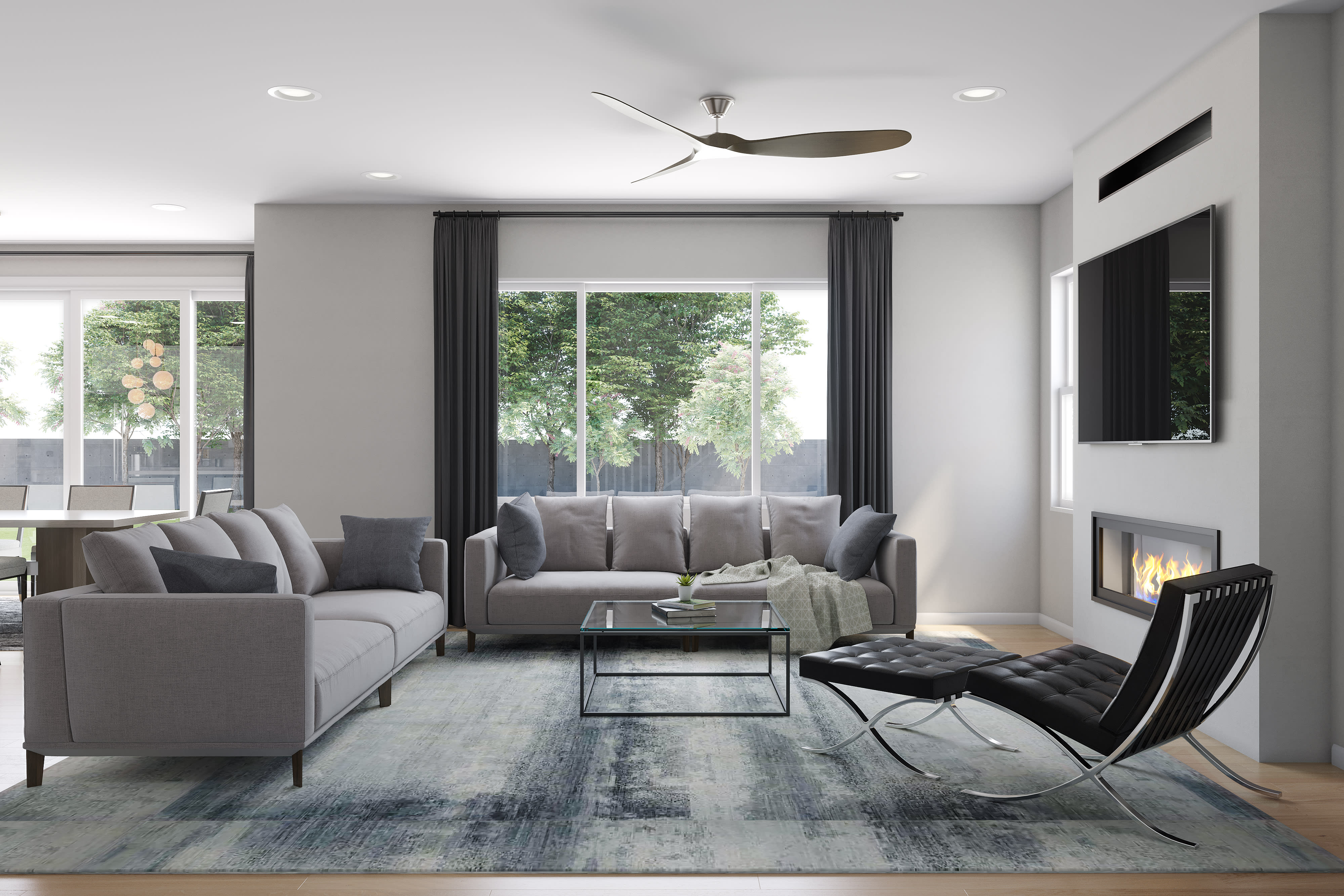 A modern and minimalist living room with gray sofas, a glass coffee table, and a Barcelona chair set against a backdrop of large windows overlooking a lush outdoor environment.