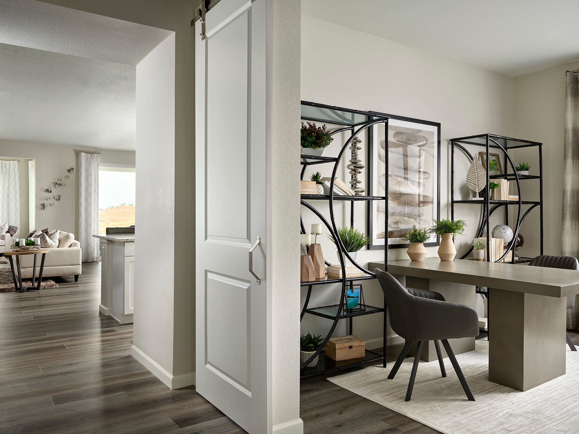 A modern and minimalist home office space with a wooden desk, a black chair, and various decorative elements such as plants and shelves on the wall.