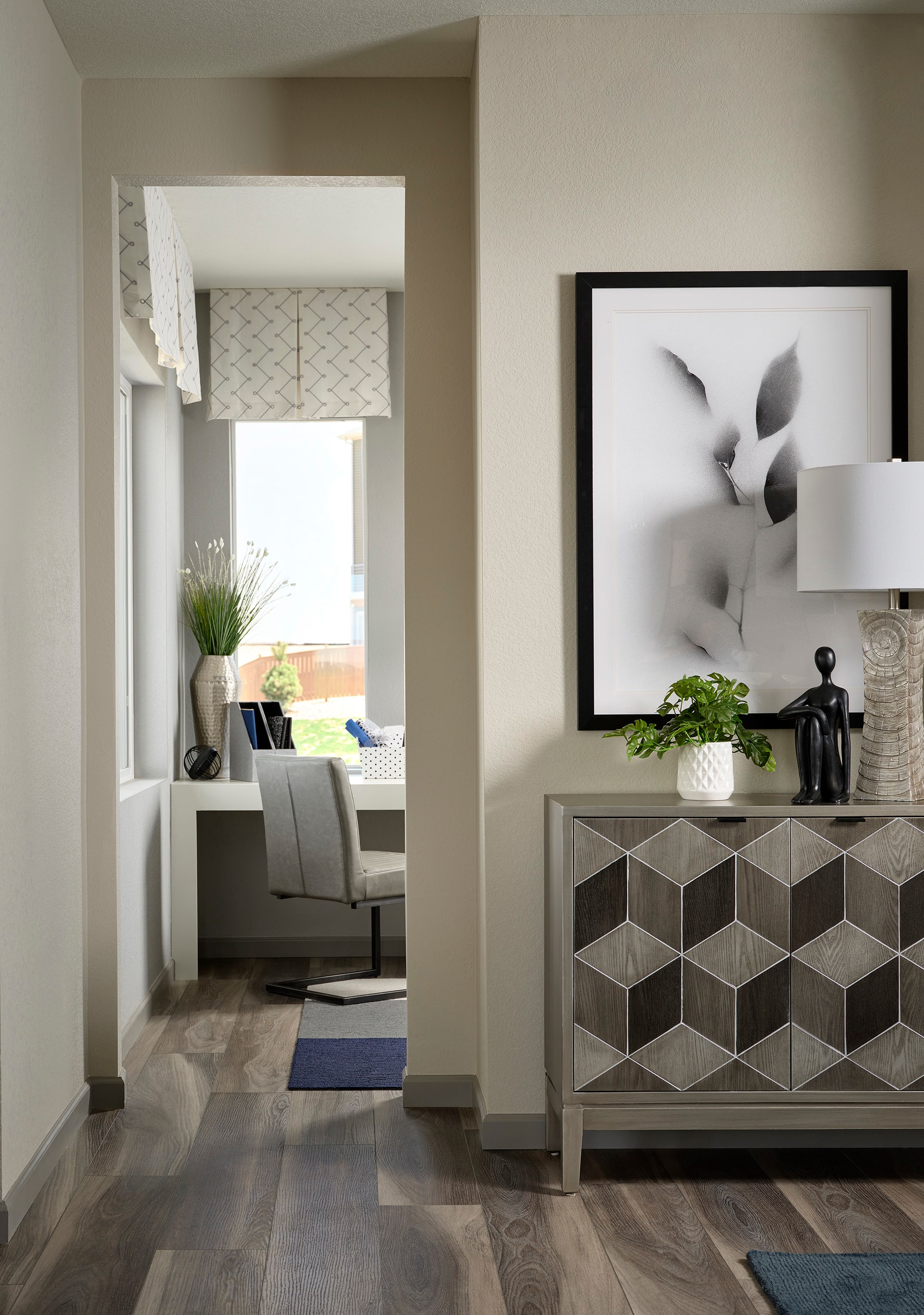 A modern and minimalist living room with a geometric patterned cabinet, a framed abstract artwork, and a cozy seating area visible in the background.