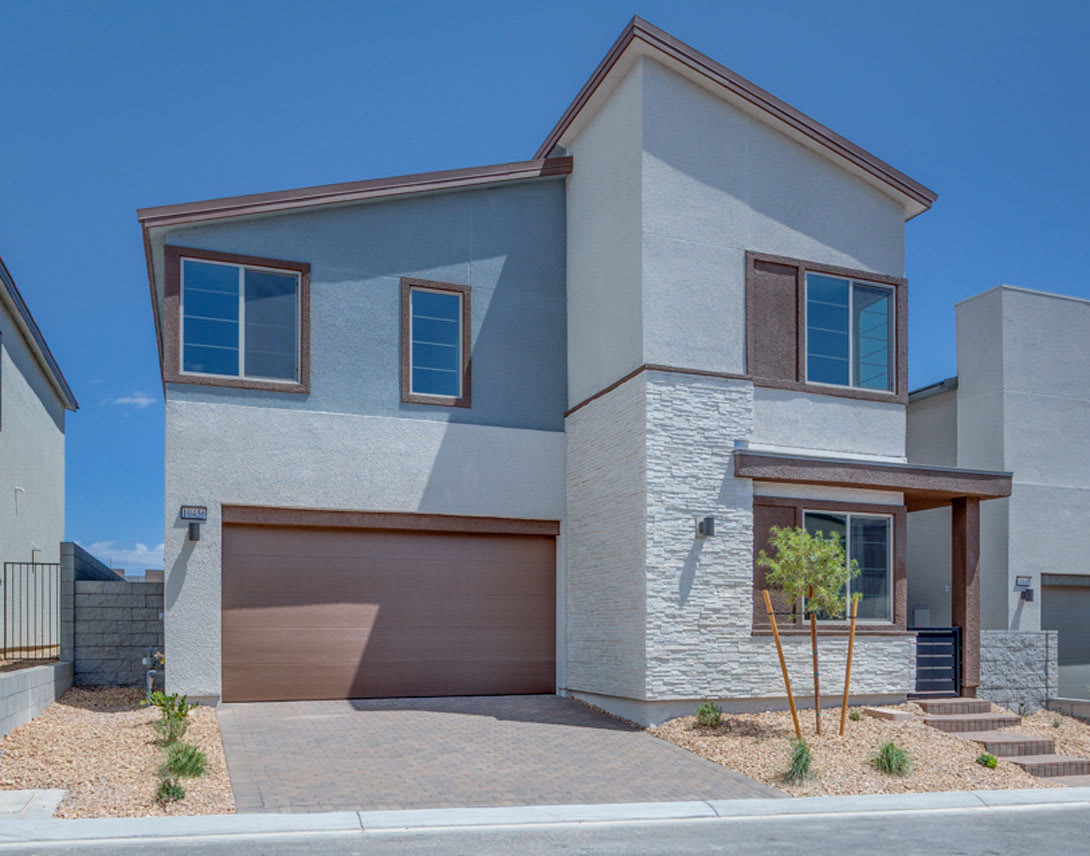 A modern two-story house with a garage, featuring a mix of gray stucco and stone exterior, set against a clear blue sky.