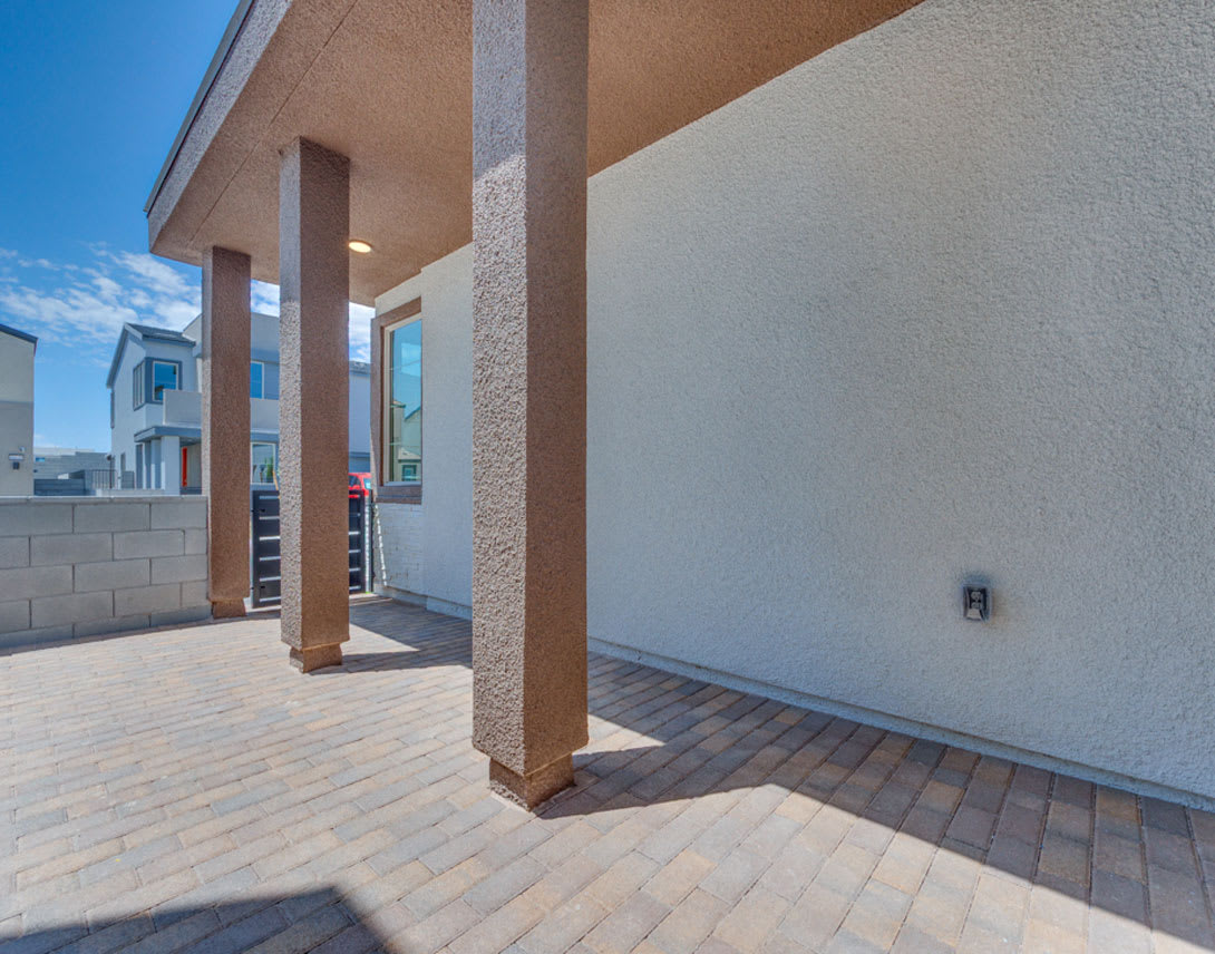 A modern, two-story building with a paved patio and wooden columns in the foreground, set against a clear blue sky in the background.