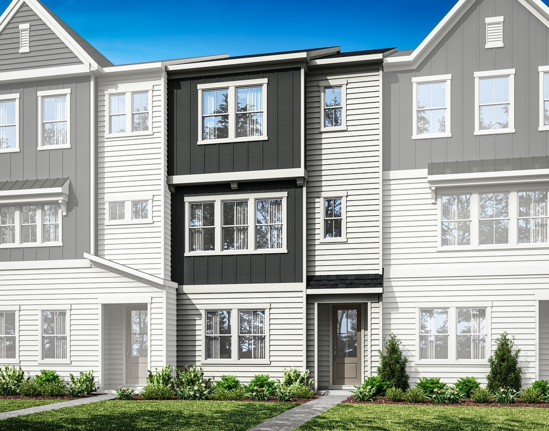 A multi-story residential building with gray siding, white trim, and a covered entryway, set against a clear blue sky with some landscaping in the foreground.
