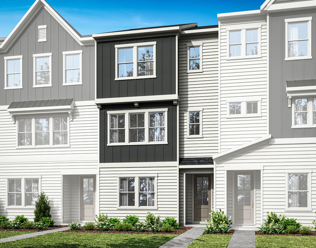 A modern, multi-story townhouse with a gray exterior and white trim, surrounded by a well-manicured lawn and landscaping, set against a clear blue sky.