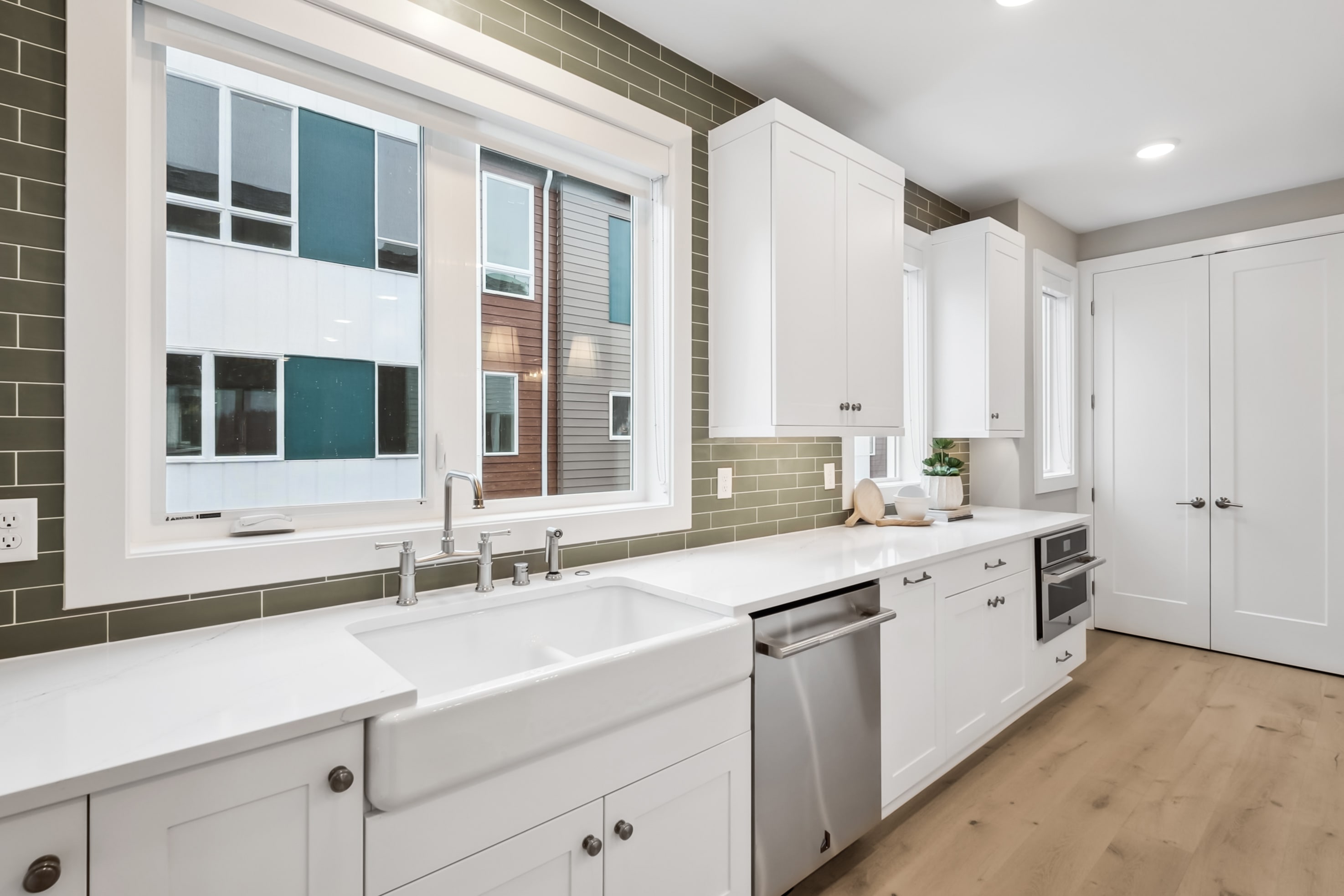 A modern, well-lit kitchen with white cabinets, a large window, and a sleek stainless steel appliance set against a backdrop of neutral-toned walls and floors.