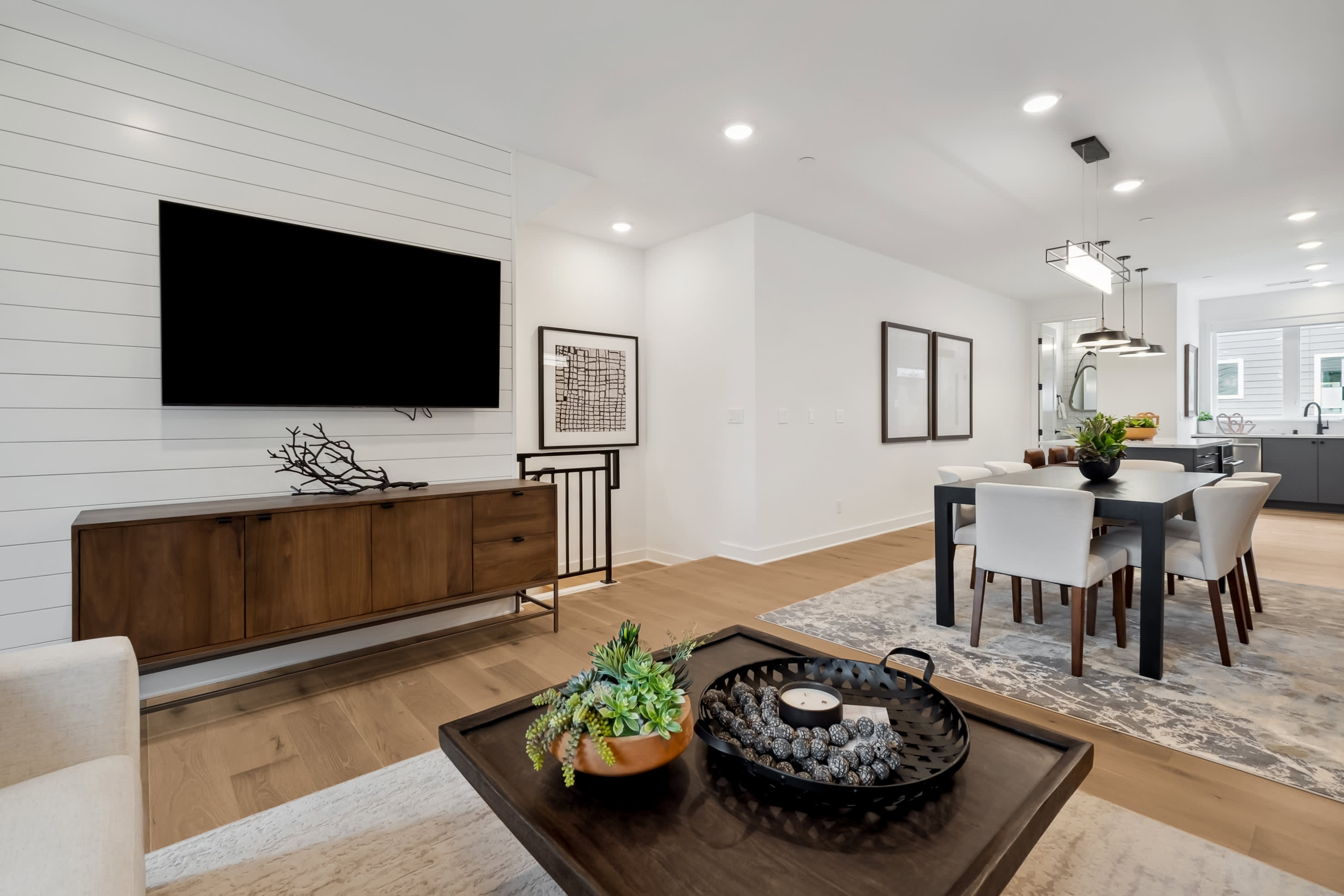 A modern and minimalist living room with a large TV, wooden furniture, and decorative elements, set against a bright and airy background.