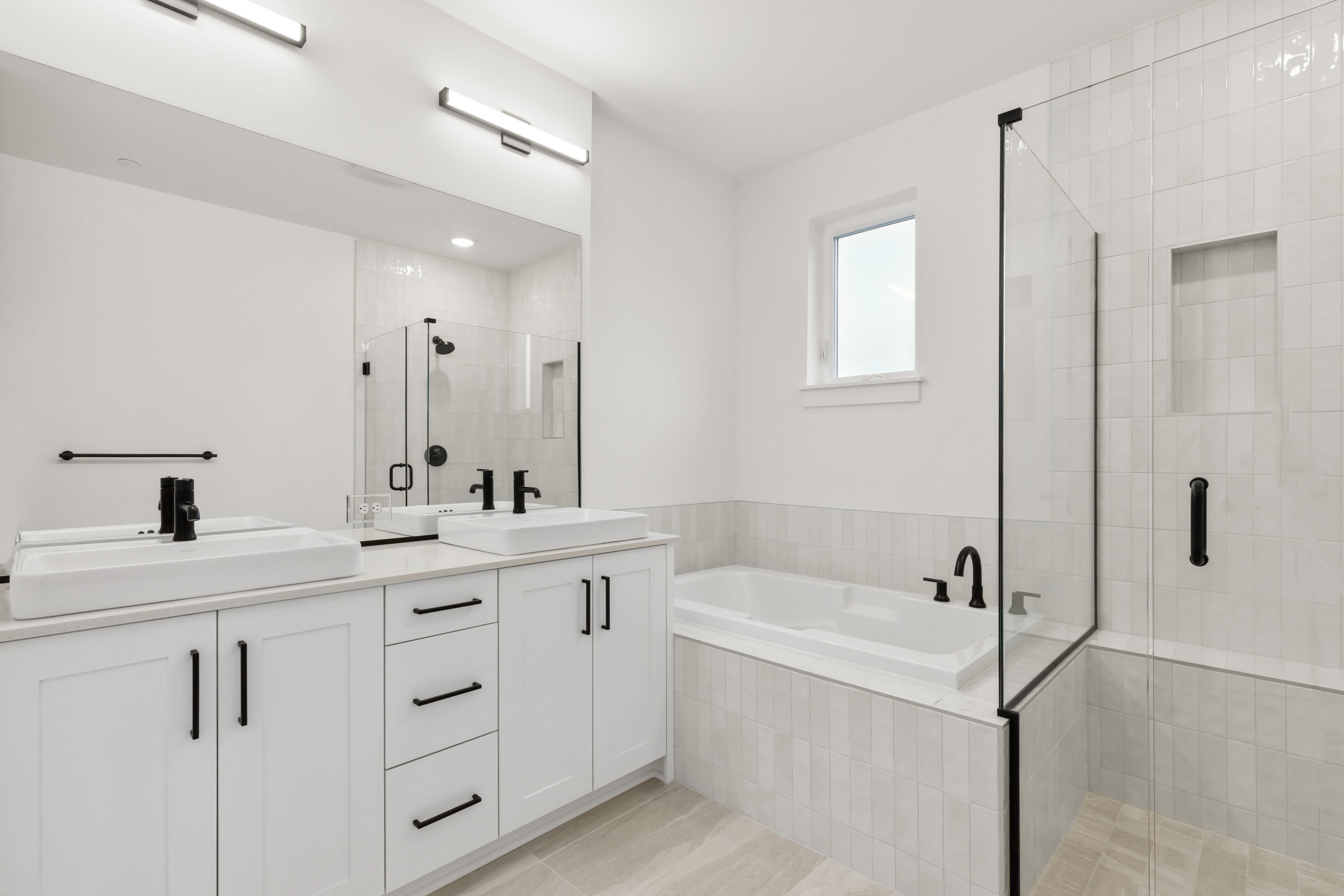 A modern, minimalist bathroom with white cabinets, a large bathtub, and a glass shower enclosure.