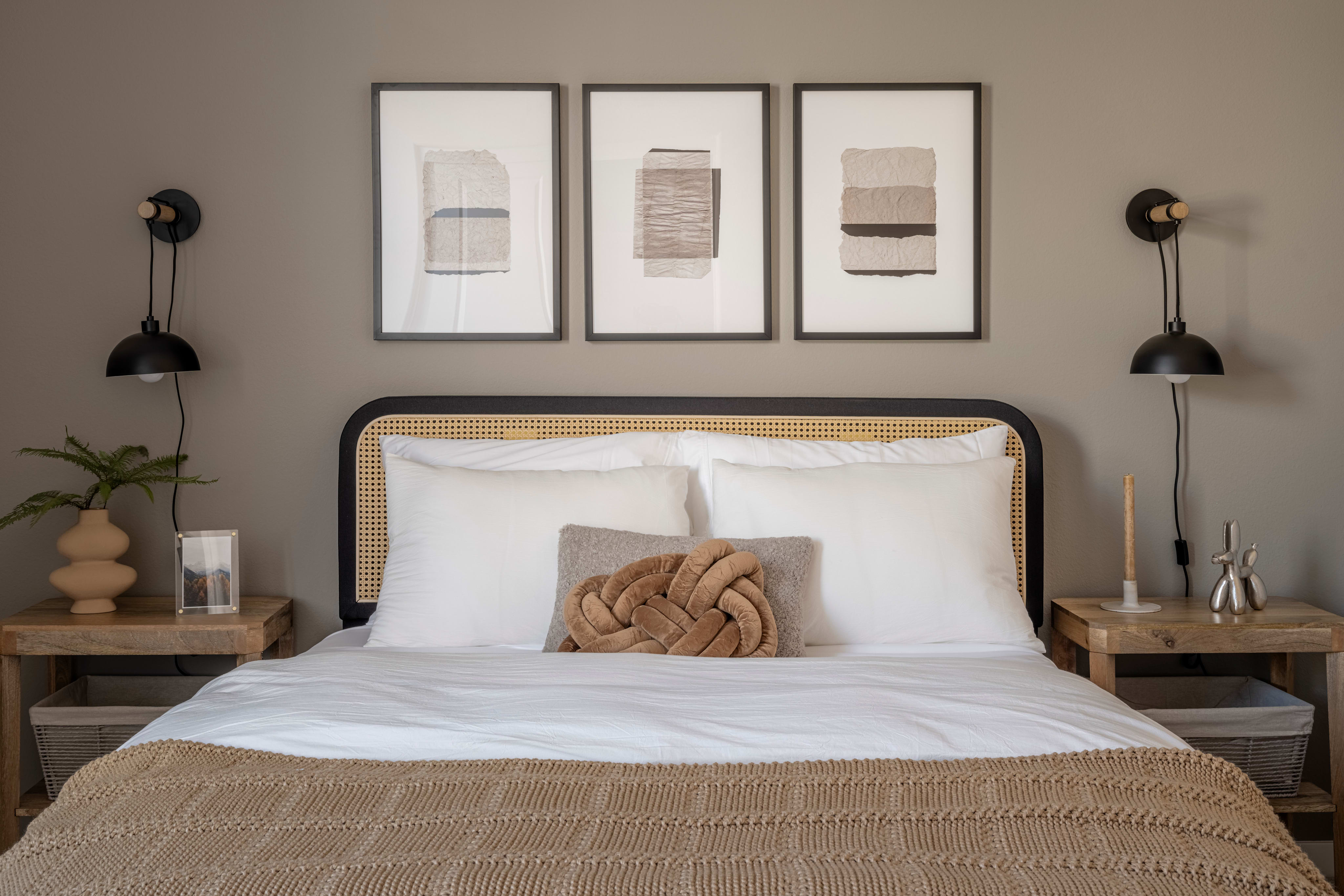 A cozy and minimalist bedroom with a white bed, wooden nightstands, and framed abstract art on the wall, creating a warm and inviting atmosphere.