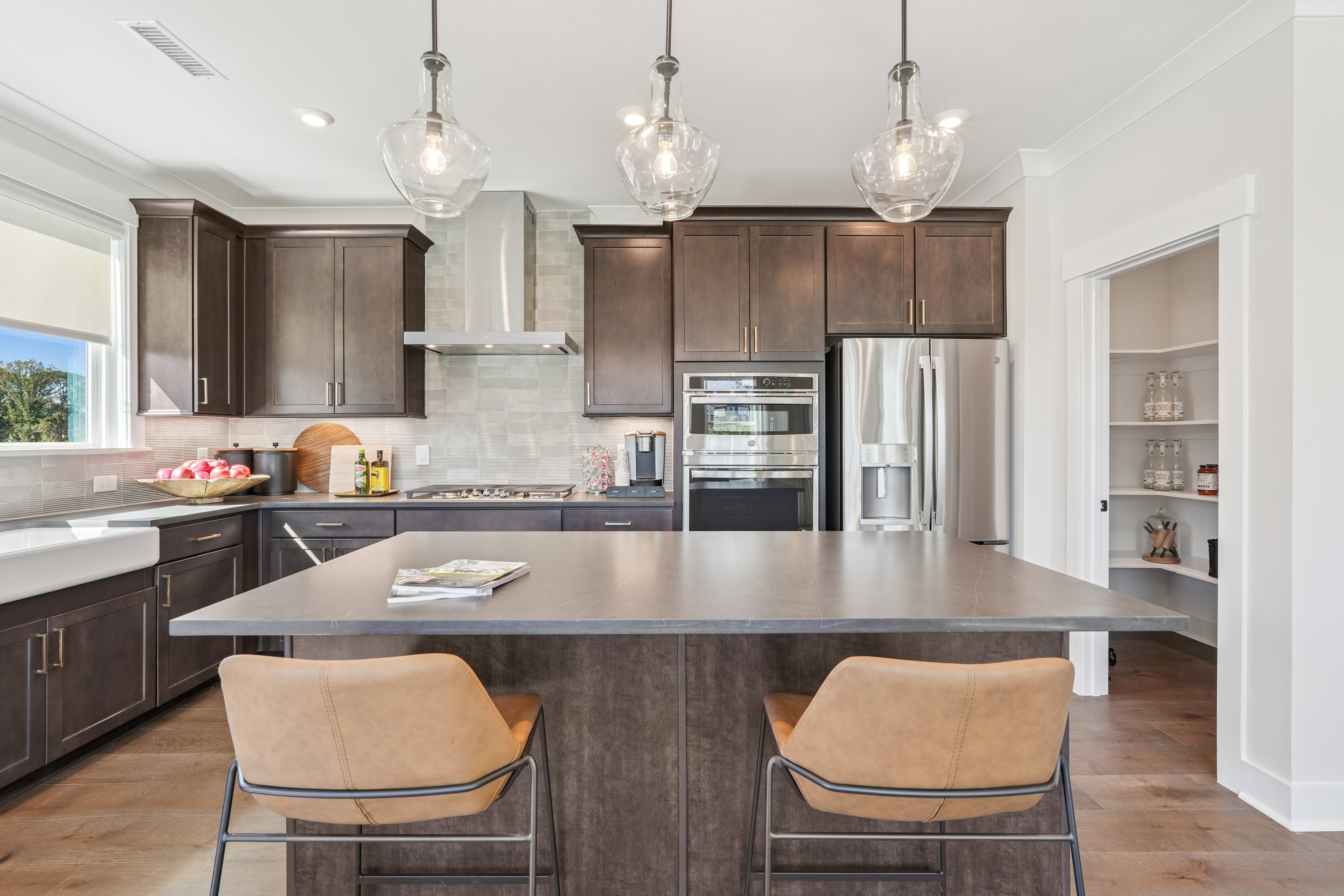 A modern and spacious kitchen with dark wood cabinets, a large island with seating, and pendant lighting fixtures hanging above.