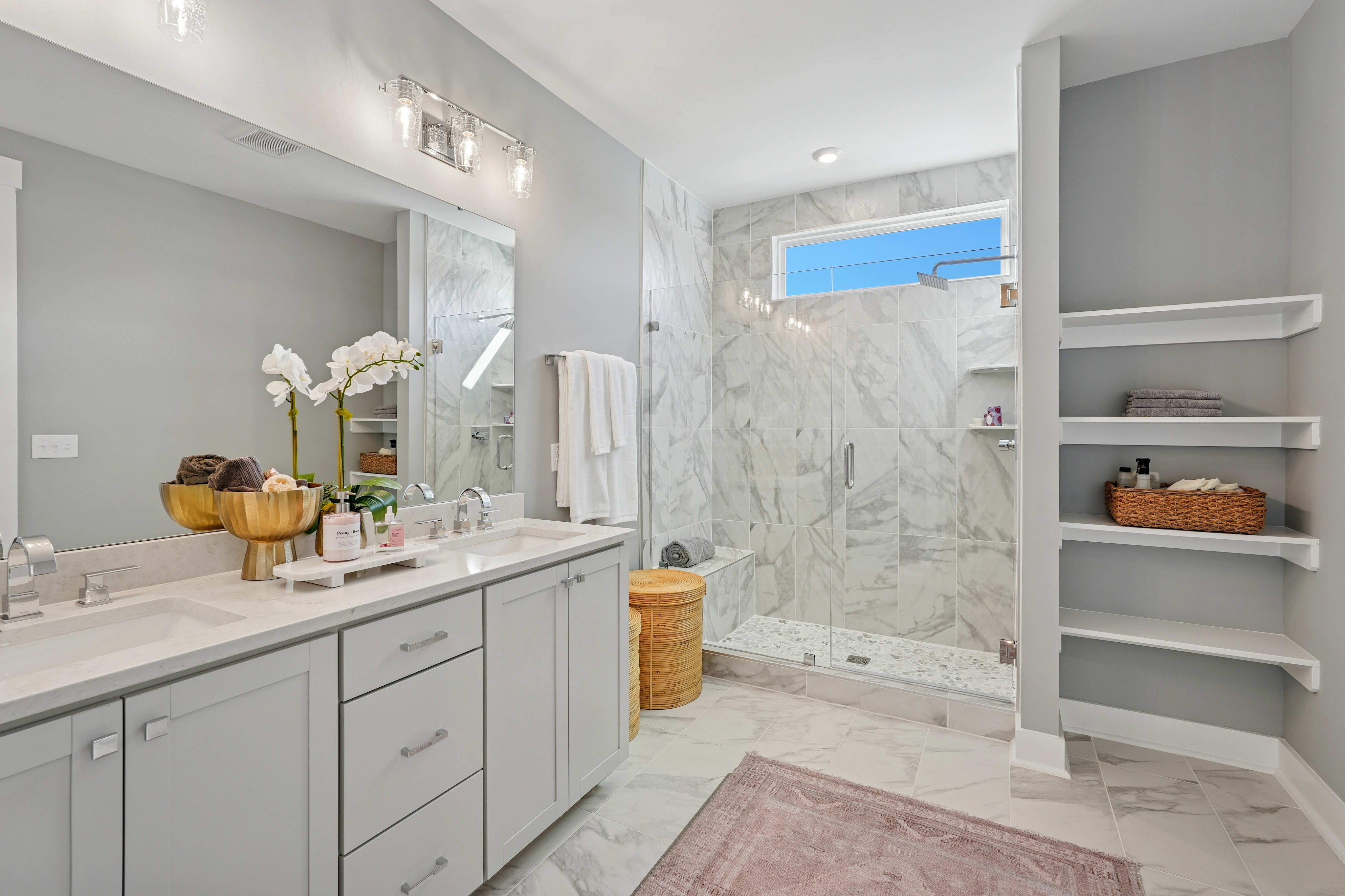 A modern and spacious bathroom with a large vanity, a walk-in shower, and shelving units for storage, all in a neutral color palette.