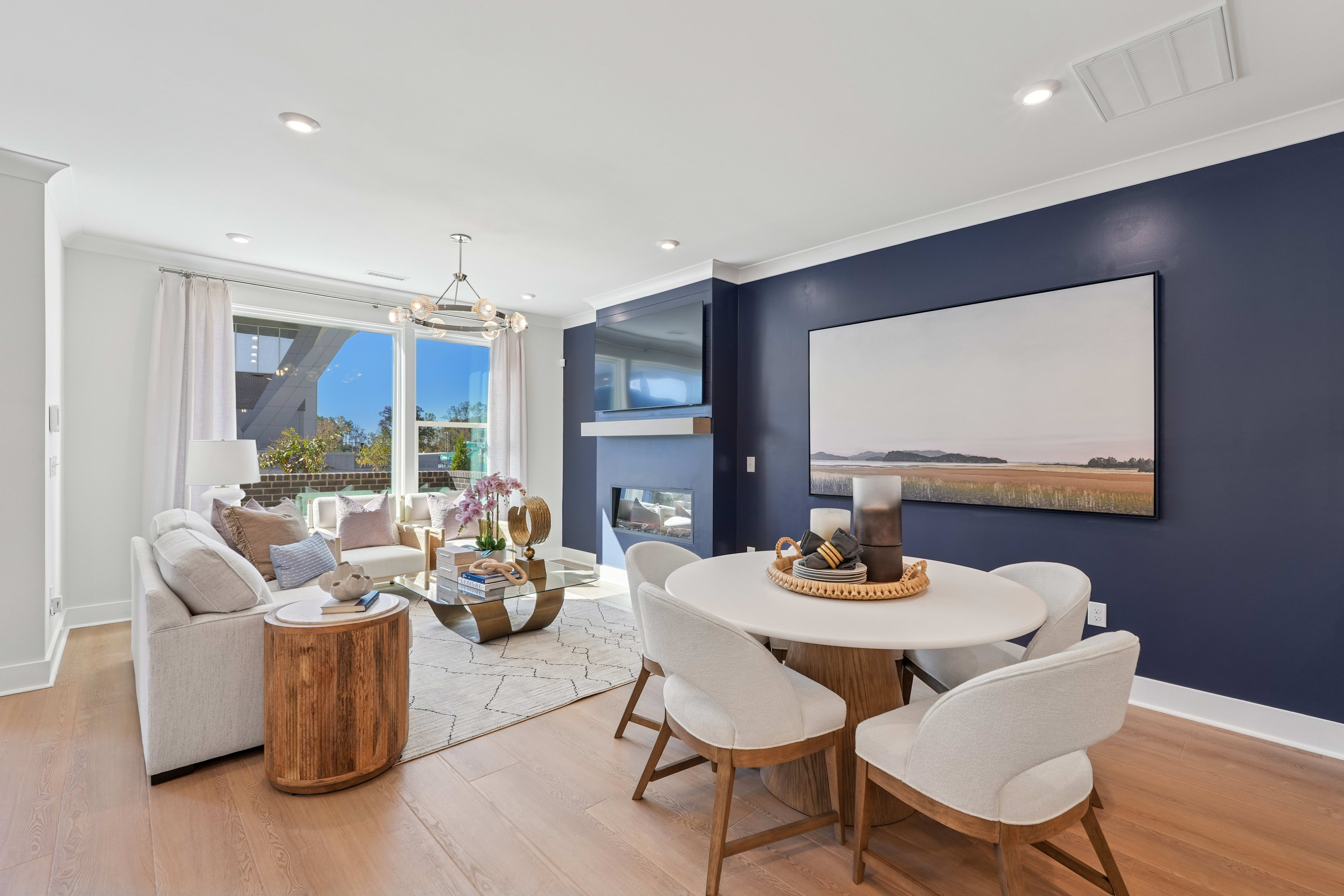 A modern and stylish living room with a dining area, featuring a large TV on the wall, comfortable white chairs, and a wooden table with decorative elements.