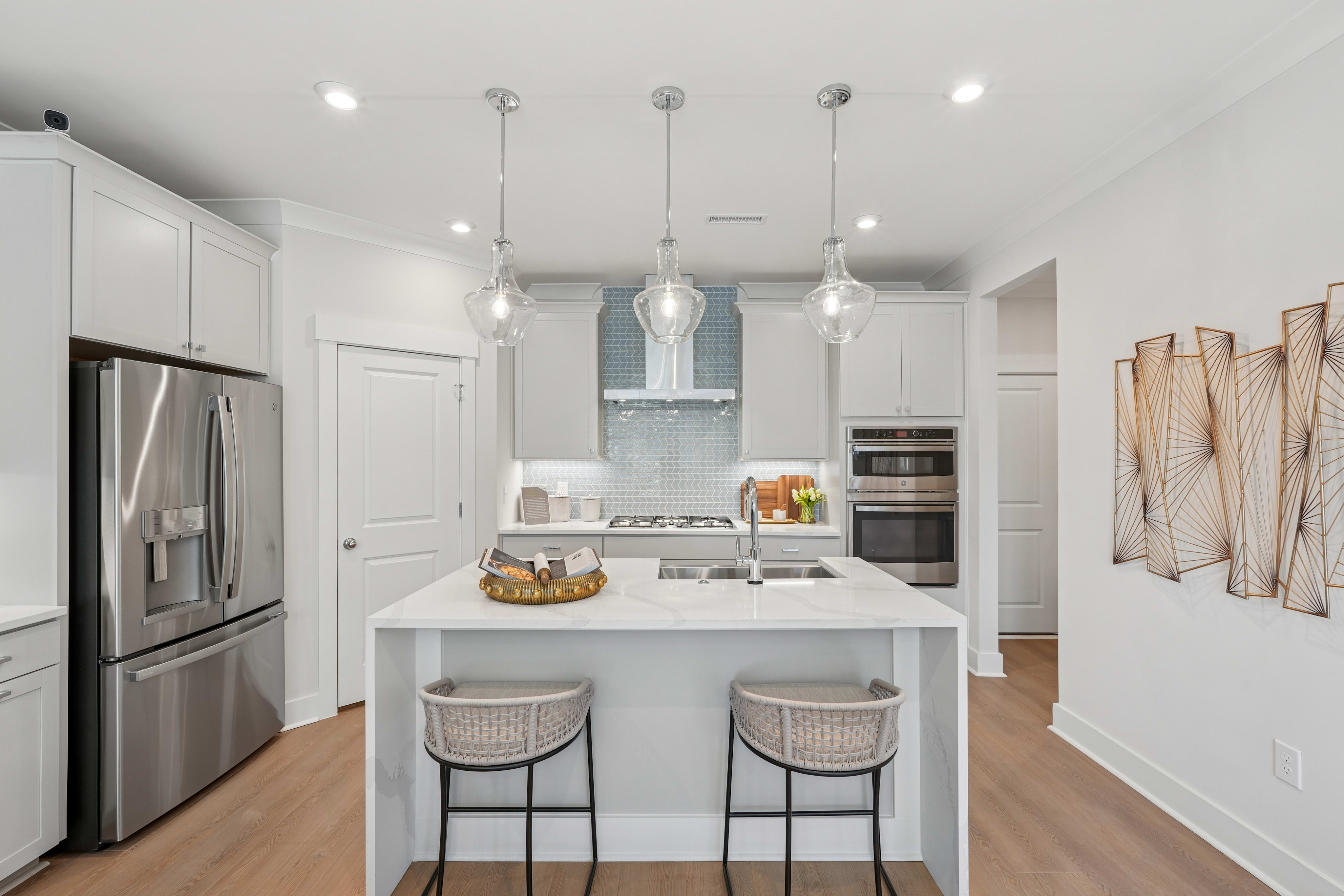A modern, well-lit kitchen with a white island, stainless steel appliances, and pendant lighting fixtures.