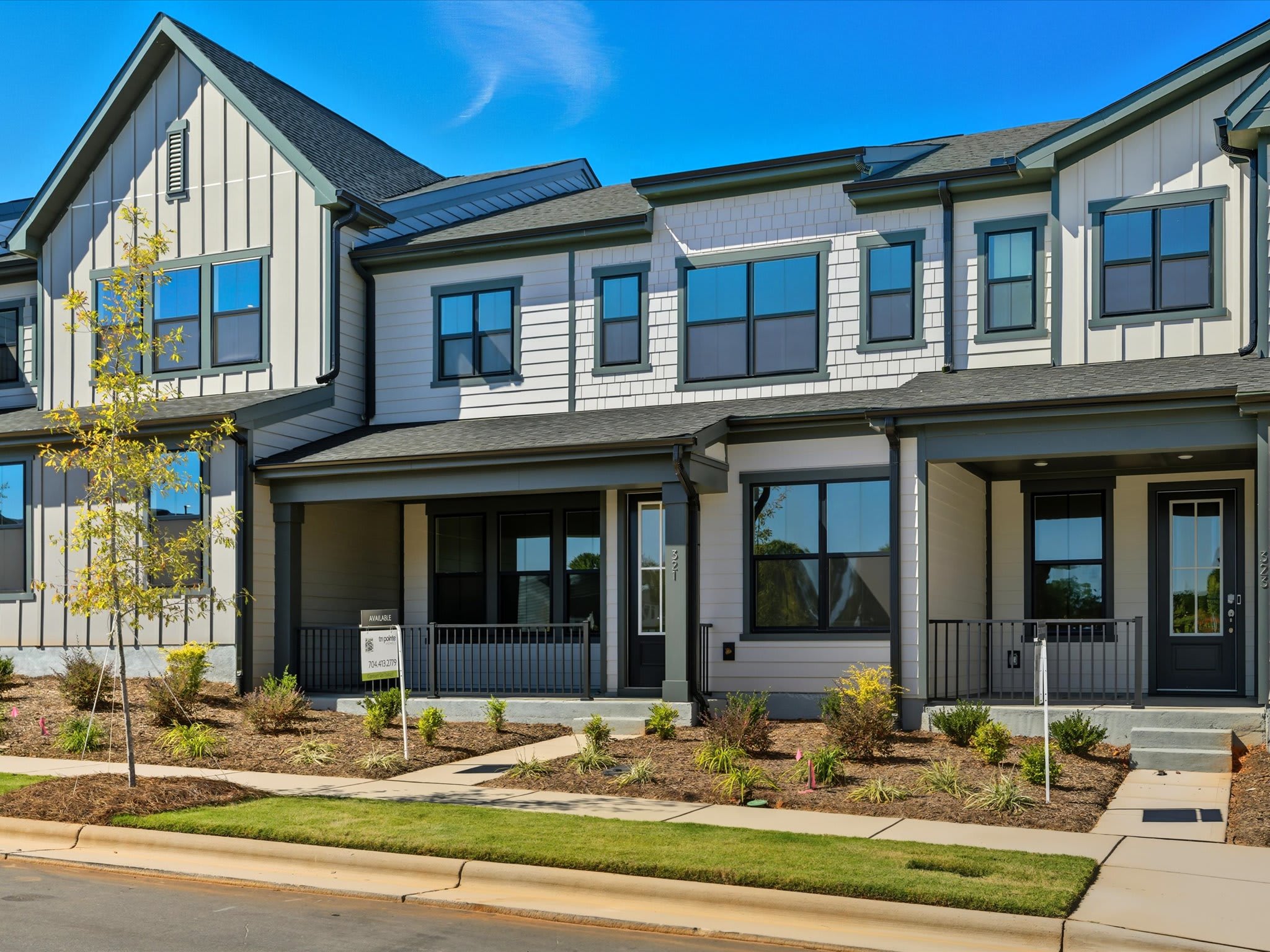 A modern, multi-story townhouse community with a well-landscaped front yard and a clear blue sky in the background.