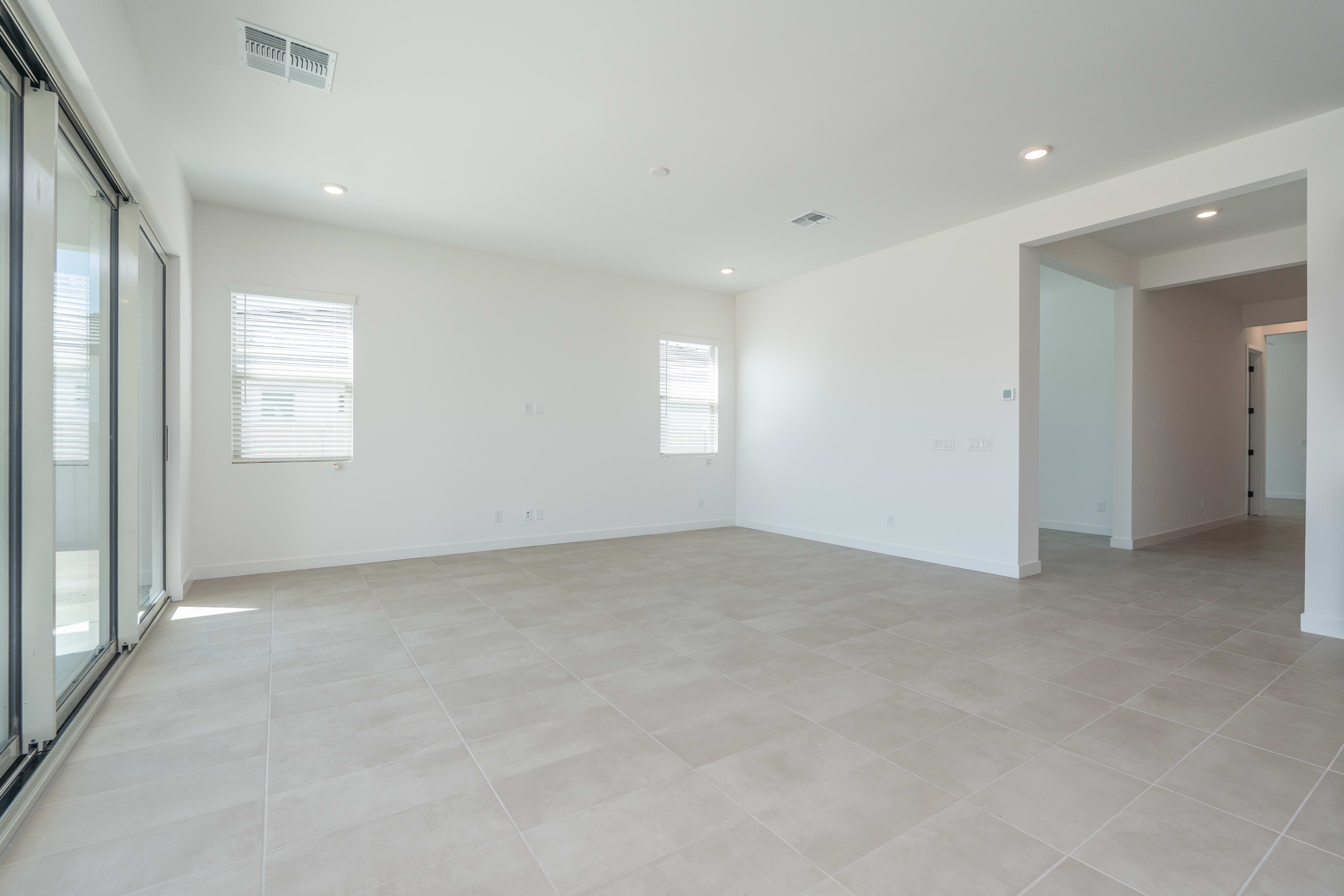 A spacious, minimalist room with large windows, light-colored tile flooring, and recessed lighting in the ceiling.
