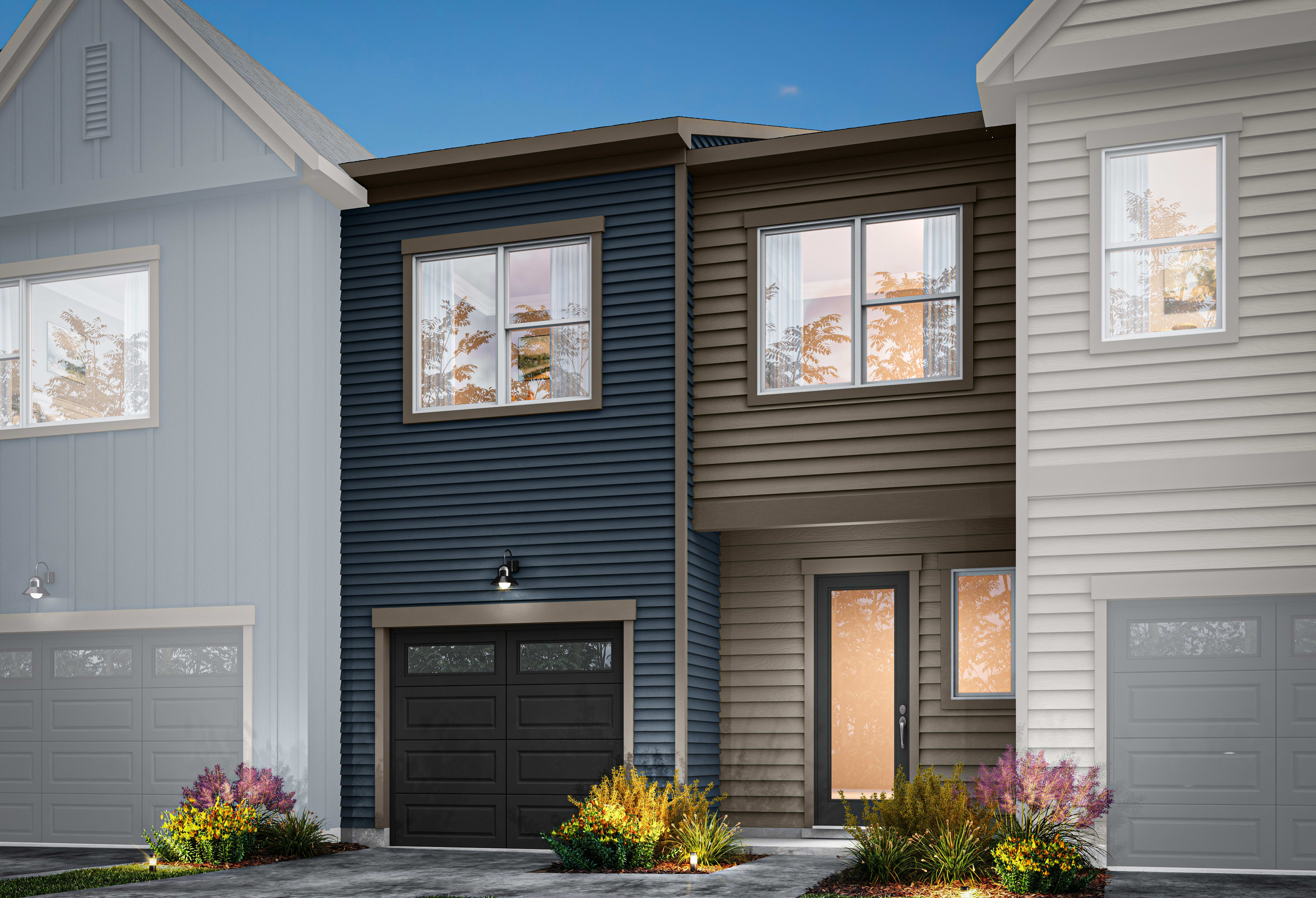 The image depicts a modern townhouse with a mix of gray and brown siding, a black garage door, and a welcoming entryway surrounded by colorful landscaping against a clear blue sky.